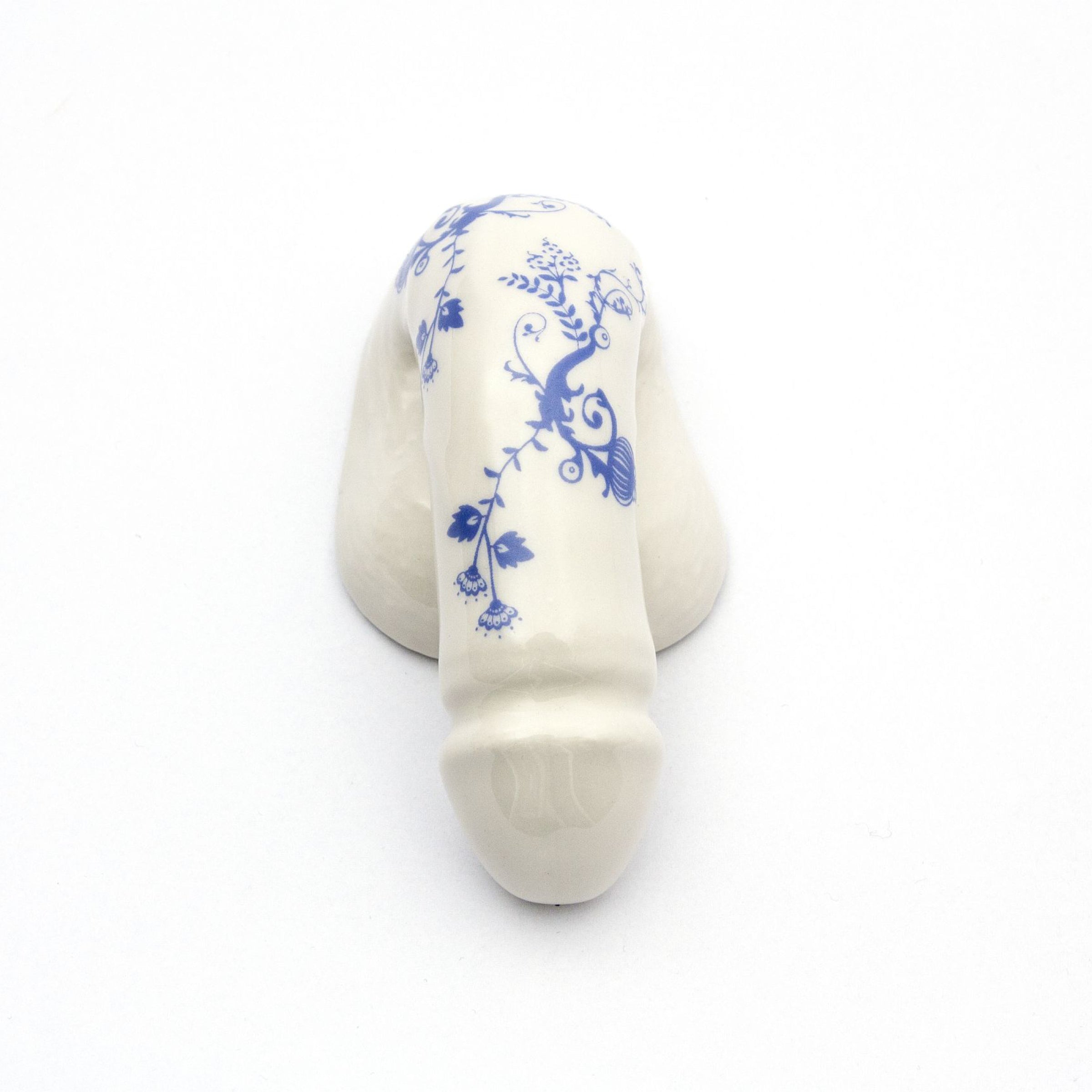 The product A Decorative Sex - Blue Onion 3 by Schwanzmanufaktur is a white porcelain piece shaped like a phallus with blue floral patterns, capturing Oscar Wildes eccentric charm, displayed on a plain white background.