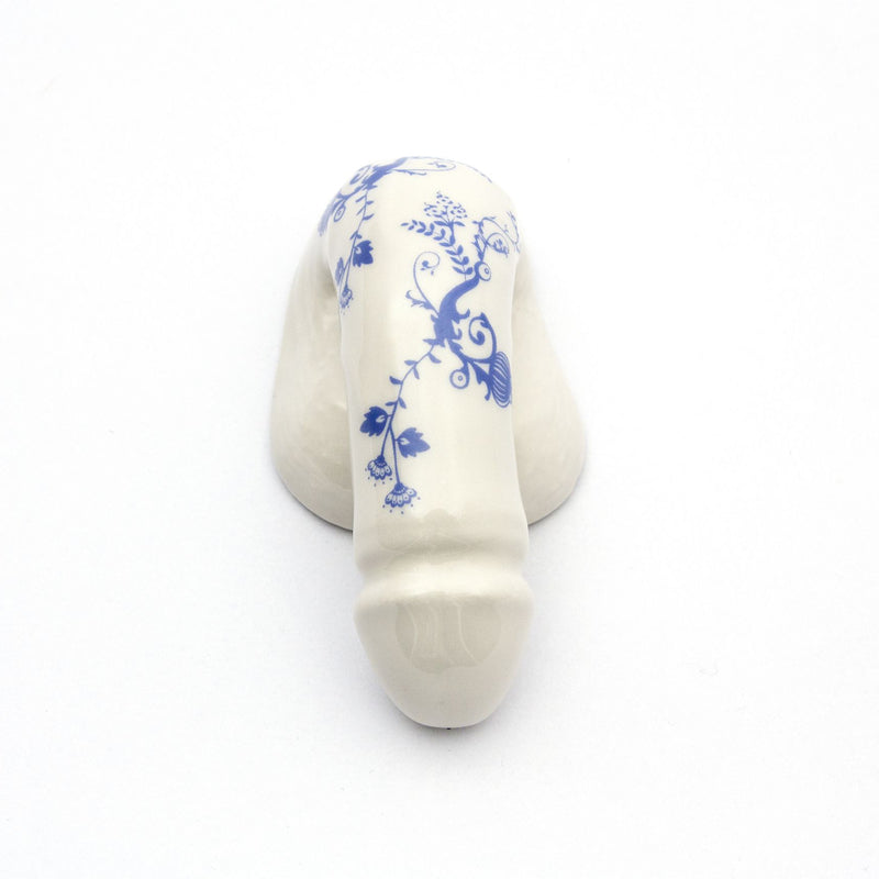 The product A Decorative Sex - Blue Onion 3 by Schwanzmanufaktur is a white porcelain piece shaped like a phallus with blue floral patterns, capturing Oscar Wildes eccentric charm, displayed on a plain white background.