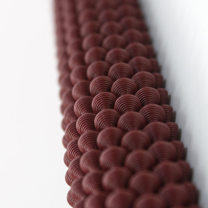 The Hoyt 29g Mezuzah by Sheyn features a close-up of textured dark red spheres, resembling precise 3D printing. The sharp details at the top blur toward the bottom, creating an evocative depth effect.