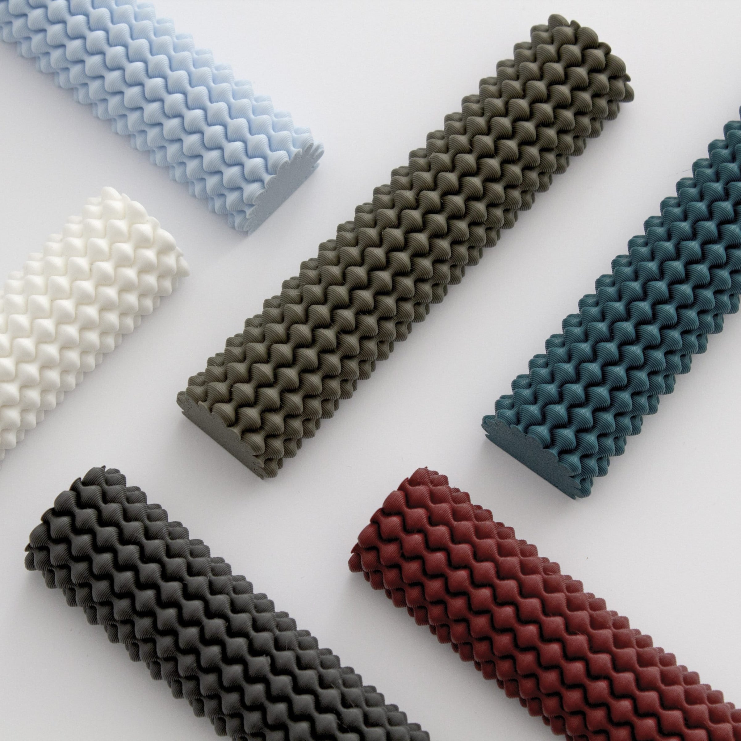 The Hoyt 29g Mezuzah by Sheyn features seven cylindrical designs with a textured zigzag pattern on a light surface, available in white, light blue, charcoal, dark gray, burgundy, teal, and dark green—reflecting the creativity and precision of 3D-printed artistry.