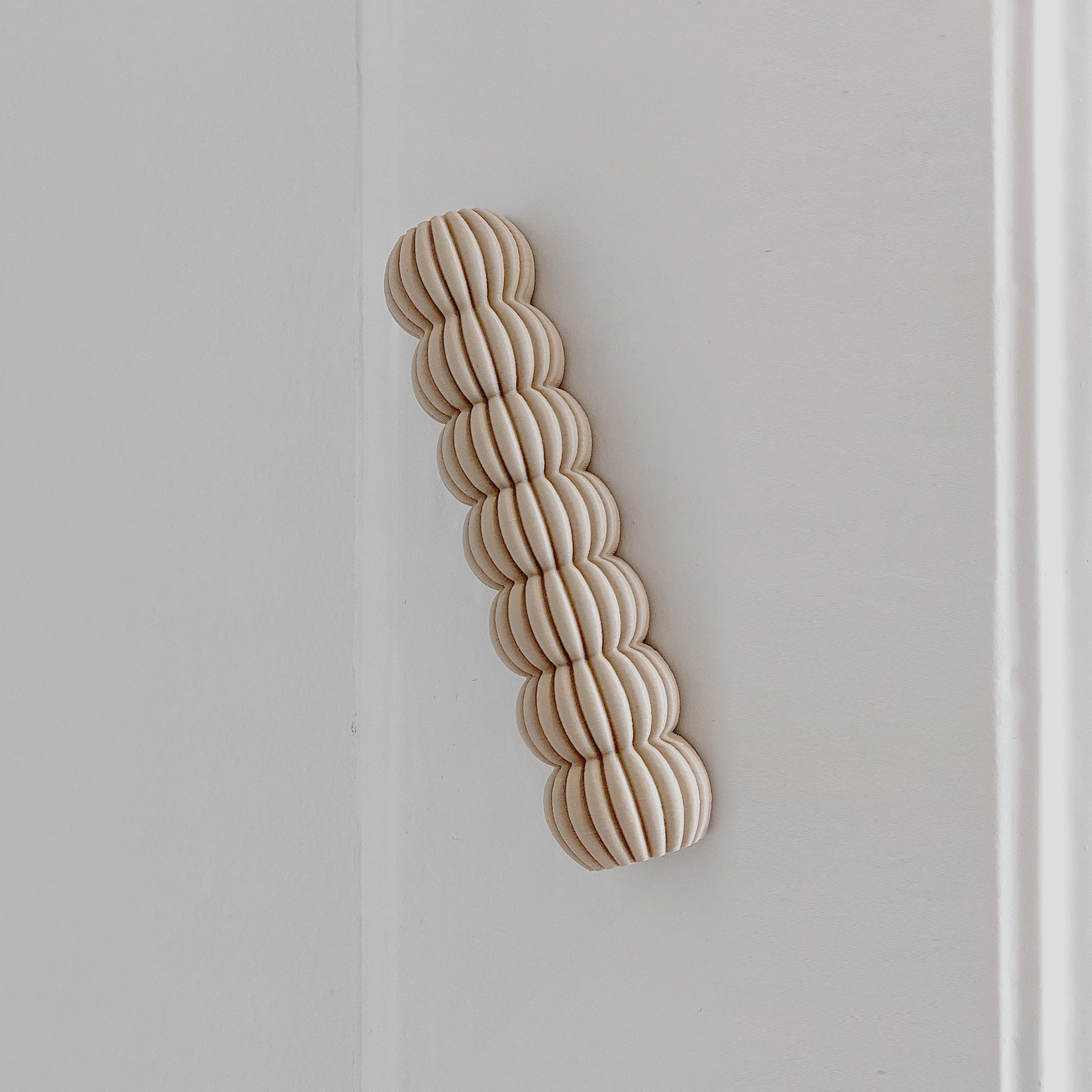 The Zayl 30g Mezuzah by Sheyn, featuring interlinked rounded wooden discs like an eco compound, is elegantly attached to a white wall in a minimalist vertical wave.