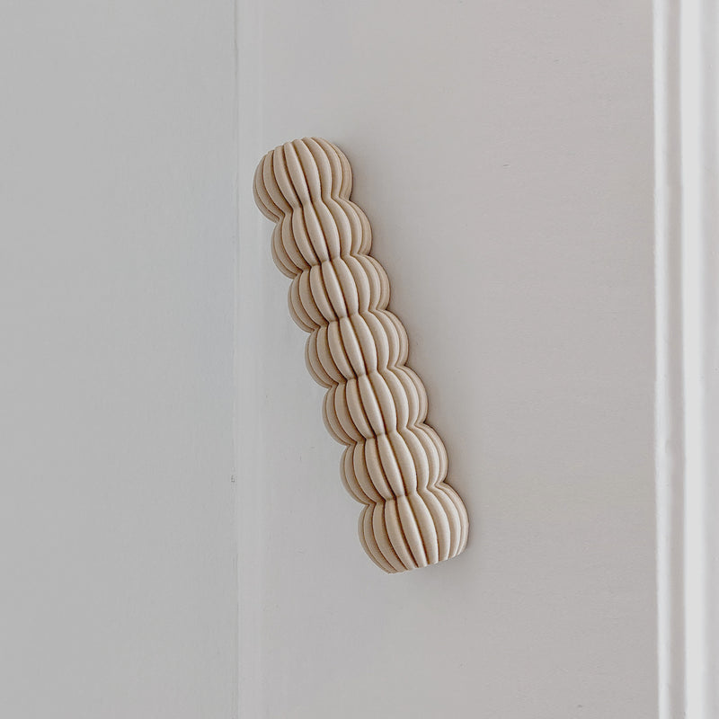 The Zayl 30g Mezuzah by Sheyn, featuring interlinked rounded wooden discs like an eco compound, is elegantly attached to a white wall in a minimalist vertical wave.