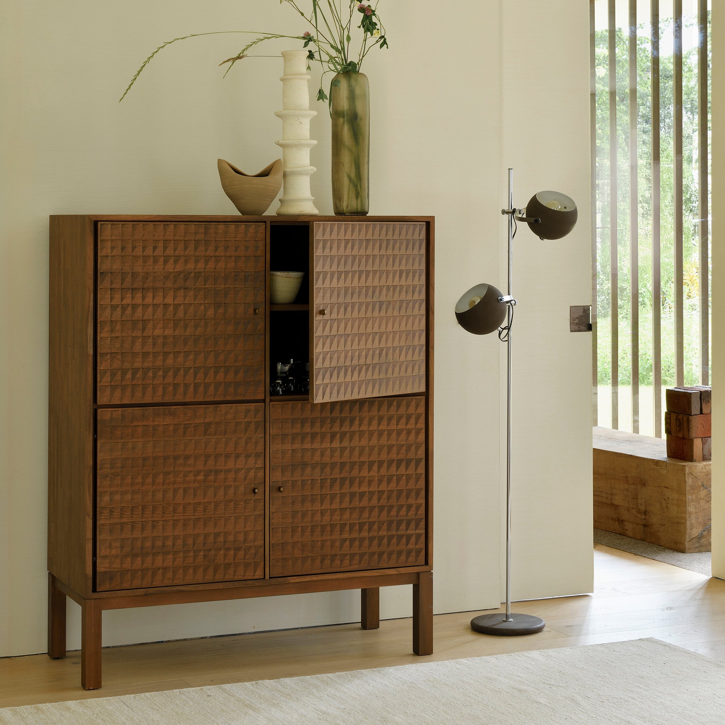 Sono Cupboard made of varnished teak with hand-carved panels and brass handles in a modern elegant room setting.