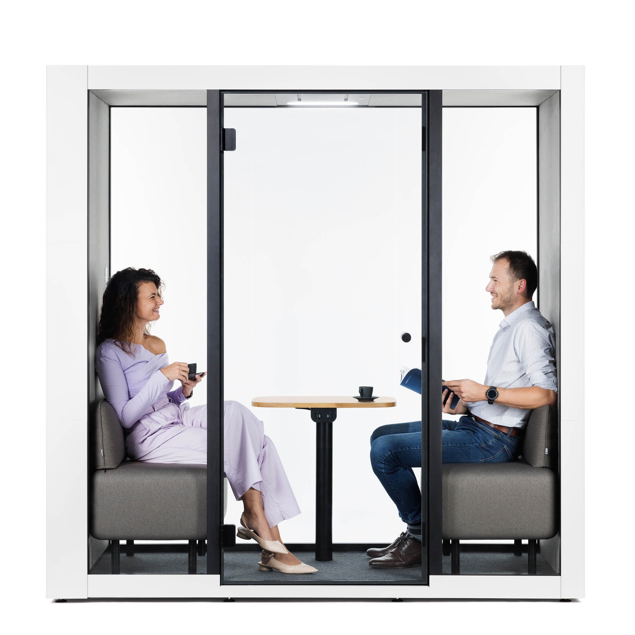 Two people sit in the SilentLab OFFICE POD SPARK 2, surrounded by ambient sounds. Theyre on opposite sides, conversing; she holds a cup, he an open book. A small table between them adds to the minimalist design and enhances working conditions.
