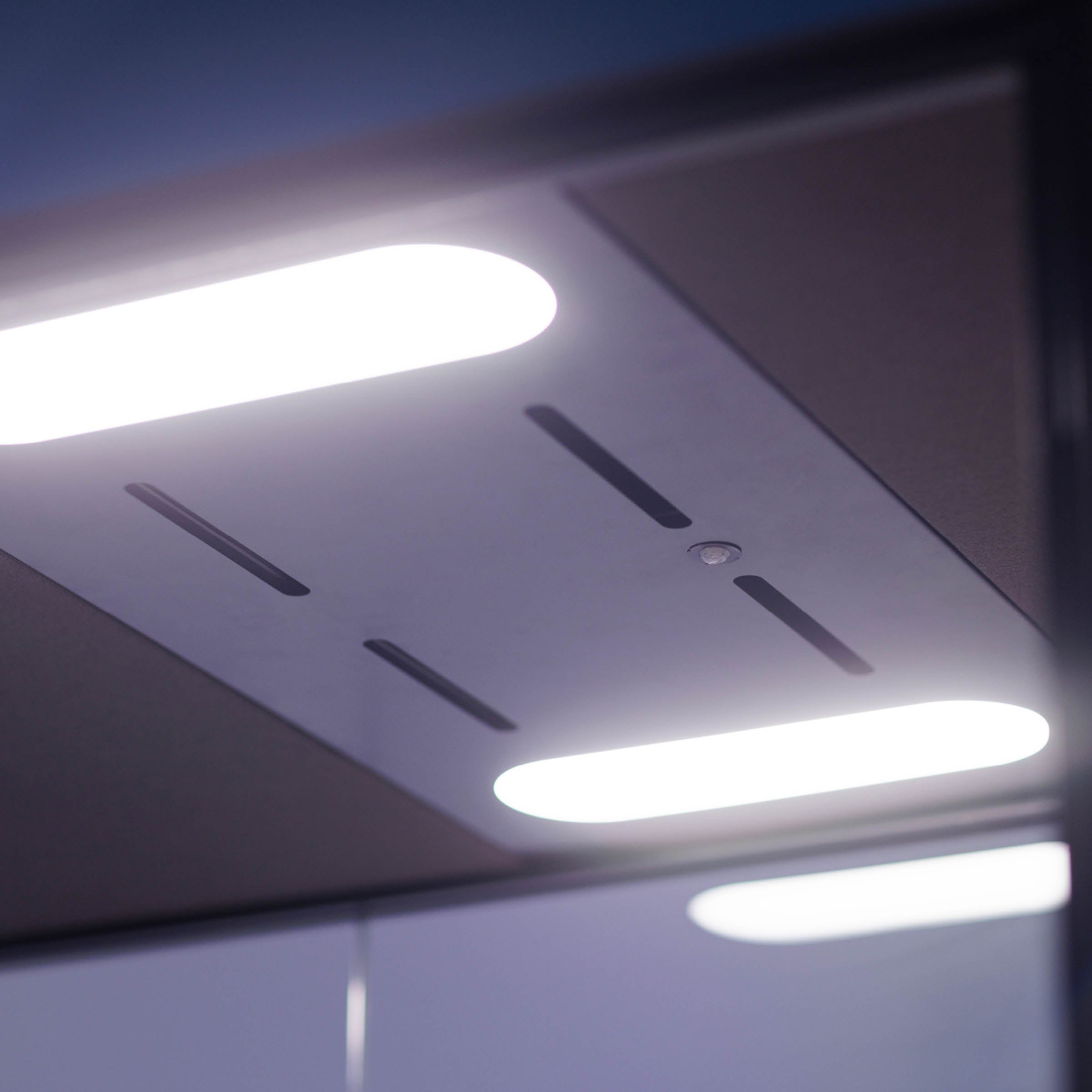 The elevator ceiling showcases three elongated, glowing oval lights that complement its modern, minimalist aesthetic with dark panels and sleek lines. Subtle ambient sounds provide a calming atmosphere similar to the SilentLab OFFICE POD SPARK 2.