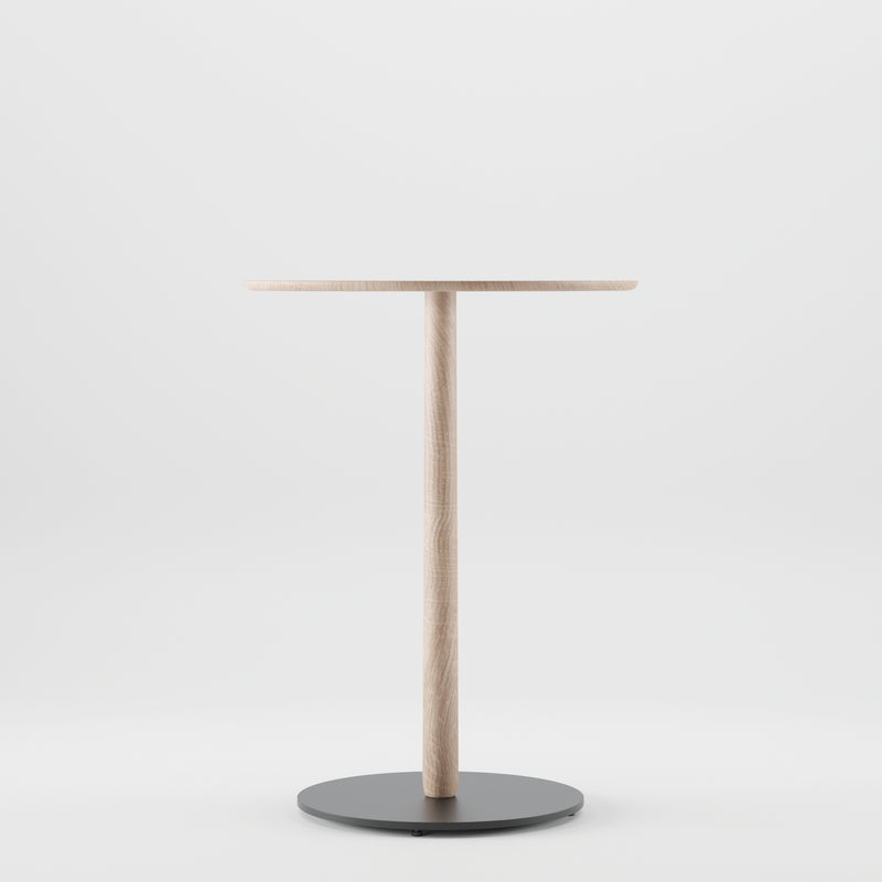 The Bistro B Table by Artisan is a minimalist wooden table, featuring a round top and single central leg made from solid wood. It rests on a circular black metal base and is enhanced by natural oils, all showcased against a plain white background with eco-friendly materials.
