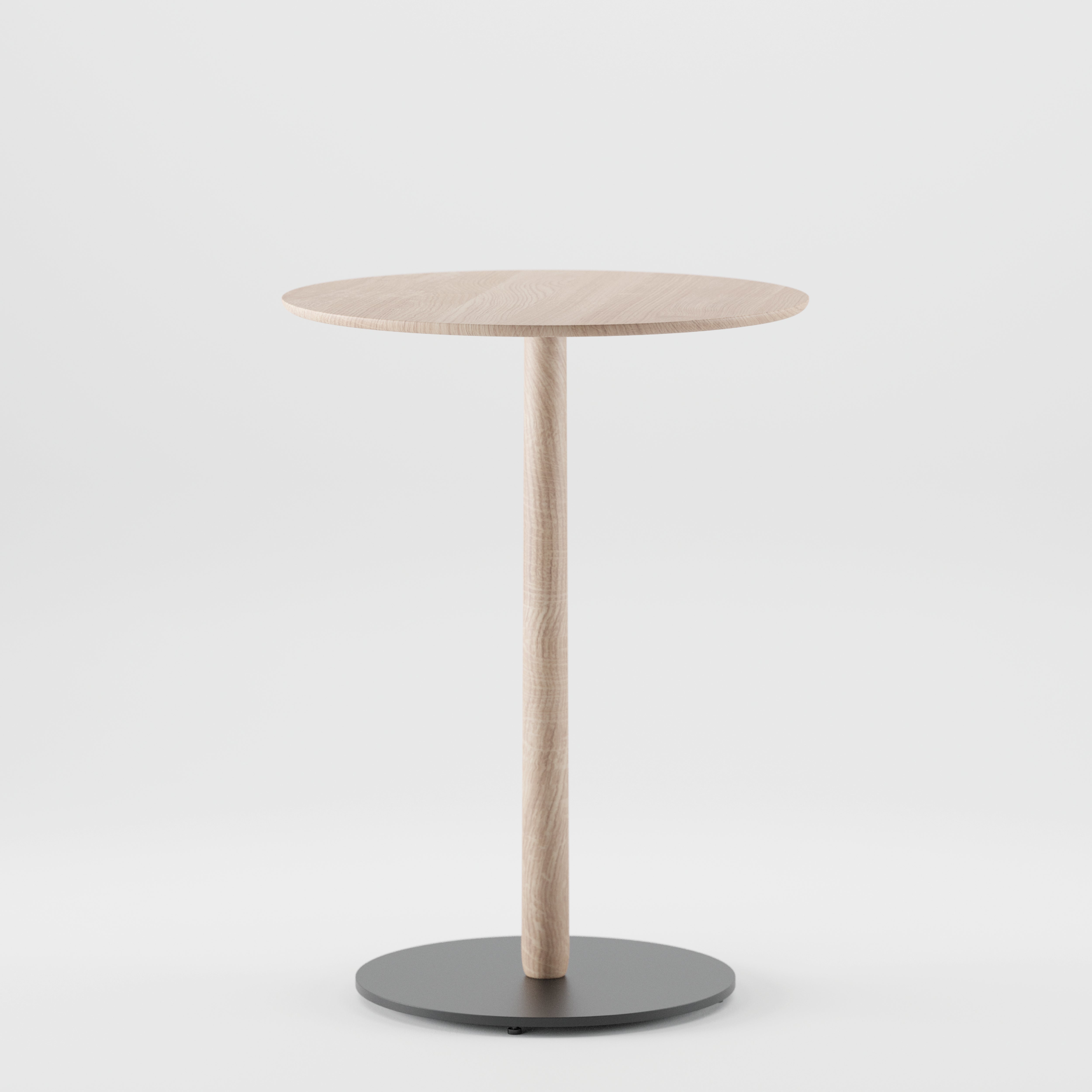 The Artisan Bistro B Table, a minimalist piece, boasts a round wooden top made from solid wood with natural oil finish. It features a thin central column and a black circular base, all set elegantly against a plain white background.