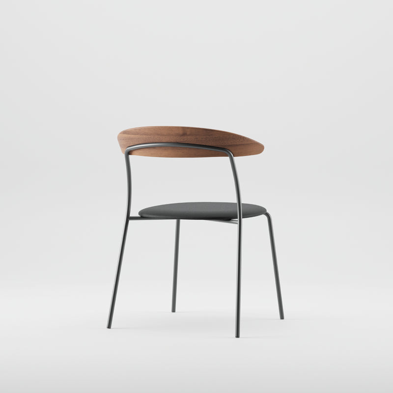 The Artisan KINU Chair boasts a modern design with a curved solid wood backrest finished in natural oils, a black cushioned seat, and sleek metal legs. Crafted from eco-friendly materials, it features minimalistic, contemporary aesthetics against a plain white background.