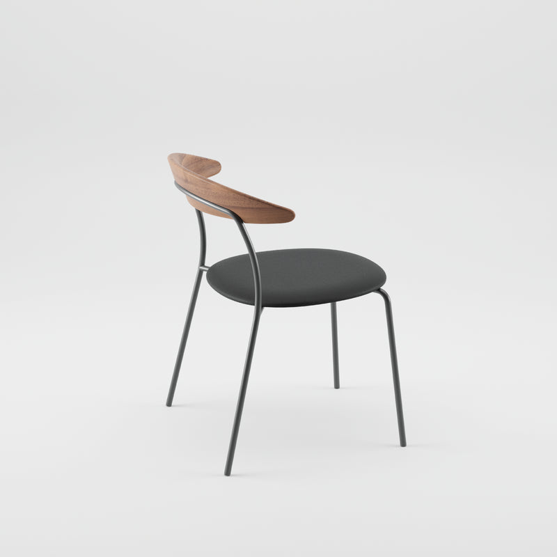The KINU Chair by Artisan showcases a minimalist design with a black cushioned seat, slender metal legs, and a curved solid wood backrest. Set against a plain white background, it exemplifies an elegant use of eco-friendly materials.