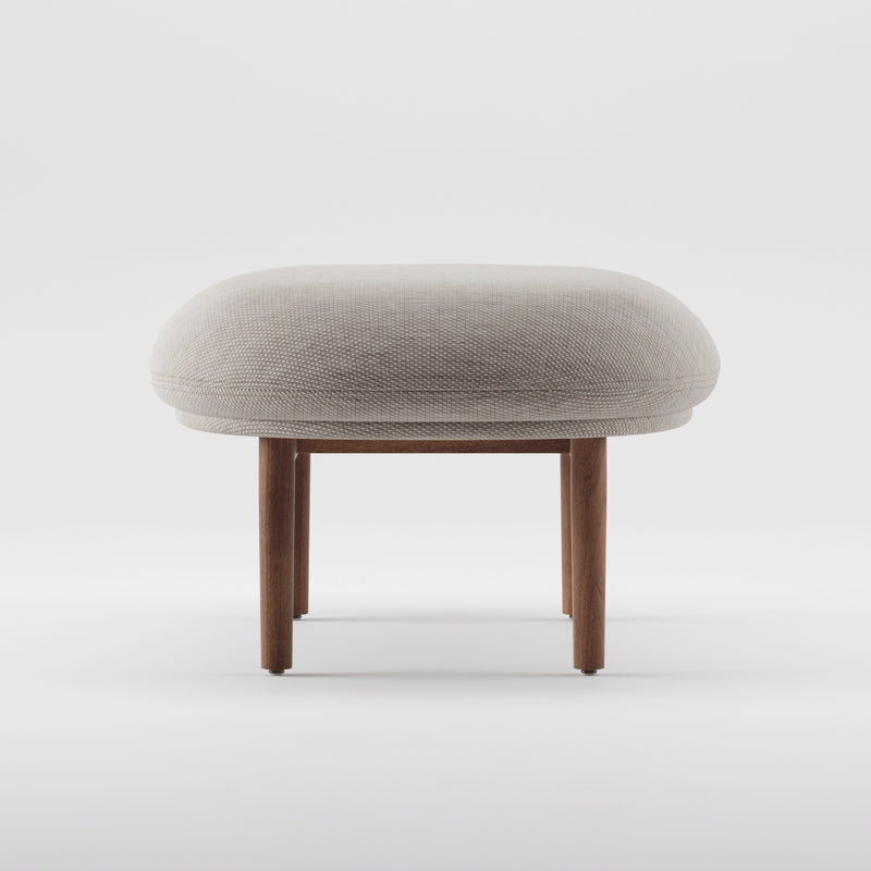 Introducing the Artisan MELA Ottoman: a minimalist piece with a round, cushioned gray seat and sturdy wooden legs. Positioned against a plain white background, it showcases its simple, modern design; featuring an elegant upholstered shell.