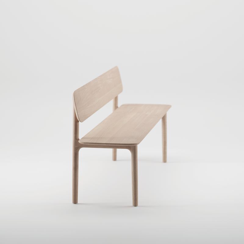 The NEVA Bench with backrest by Artisan is minimalist, featuring a sleek design with light wood and four slim legs, set against a white background. Crafted using CNC carving techniques, it offers a modern look.