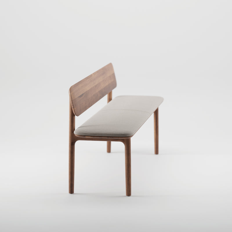 The NEVA Bench with backrest by Artisan is a minimalist wooden piece with a light gray cushion on both seat and backrest. Its contemporary, sleek design showcases the skill of artisan carpenters against a plain white background.