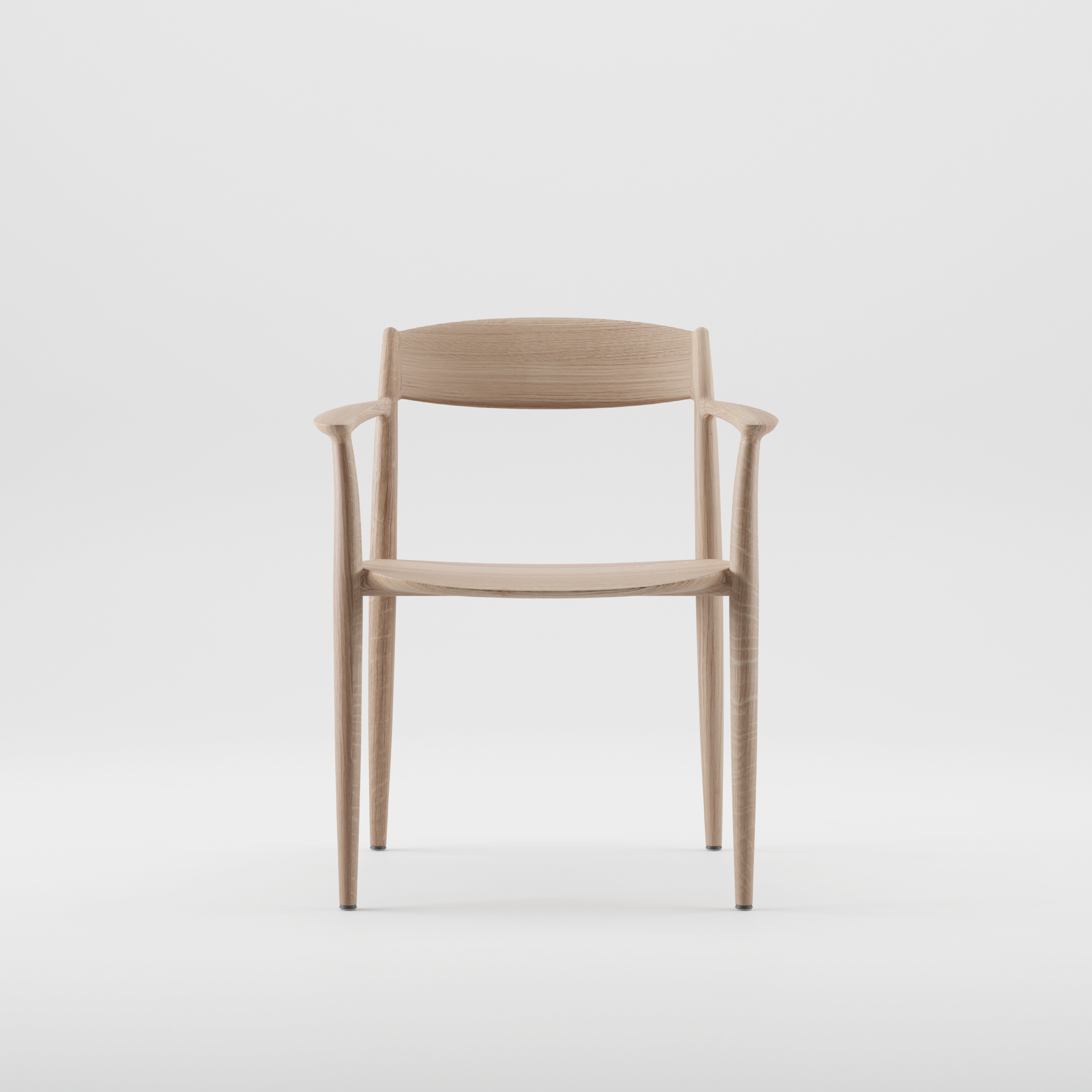 The NILA Chair by Artisan is a minimalist piece crafted from solid wood with a natural finish. It features a curved backrest and armrests, four straight legs, and is enhanced by natural oils. The chair is showcased against a plain white background.