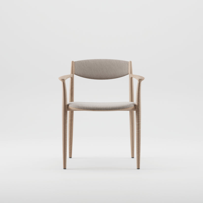 The NILA Chair by Artisan is a minimalist wooden chair made from solid wood. It features a light grey cushioned seat and backrest, sleek curved armrests, and tapered legs. Highlighting its environmentally-friendly materials, it stands out against a plain white background.