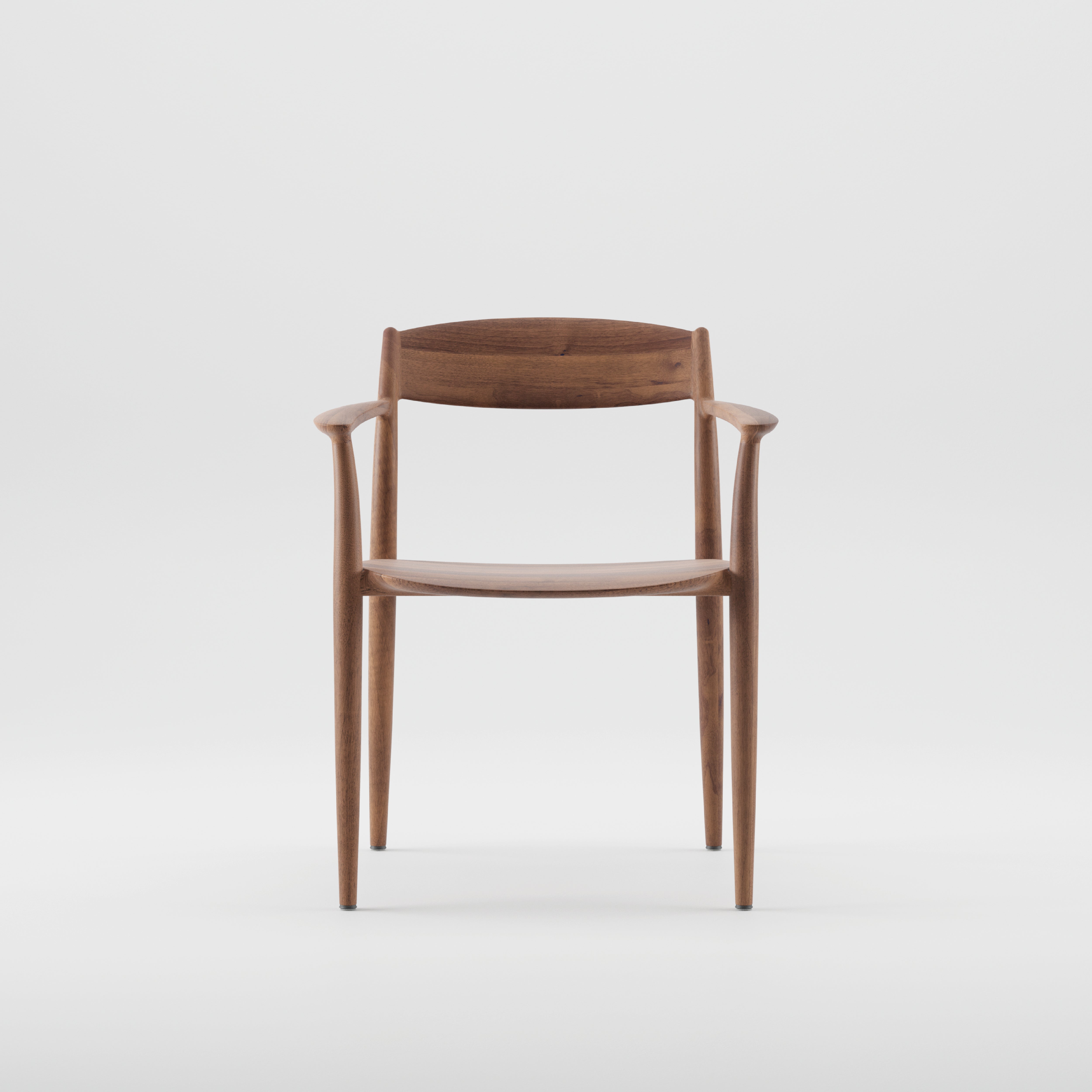 The NILA Chair by Artisan showcases a sleek, minimalist design with a curved backrest and smooth armrests. Crafted from solid wood and finished with natural oils, it features tapered legs in rich dark wood, all set against a plain white background.