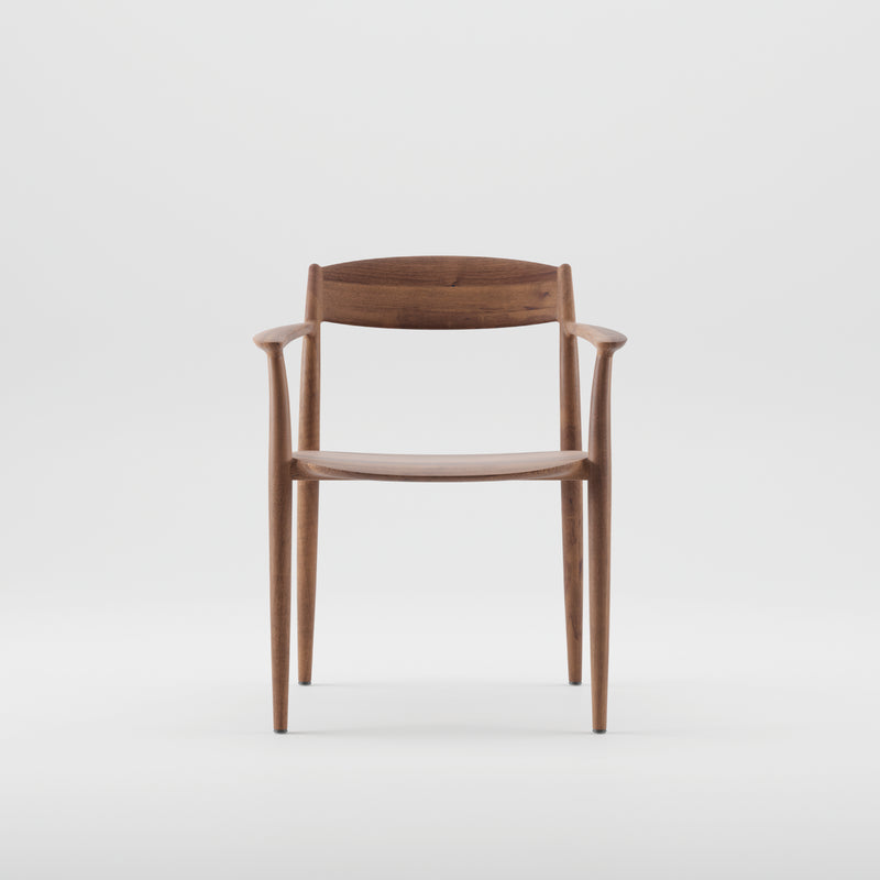 The NILA Chair by Artisan showcases a sleek, minimalist design with a curved backrest and smooth armrests. Crafted from solid wood and finished with natural oils, it features tapered legs in rich dark wood, all set against a plain white background.