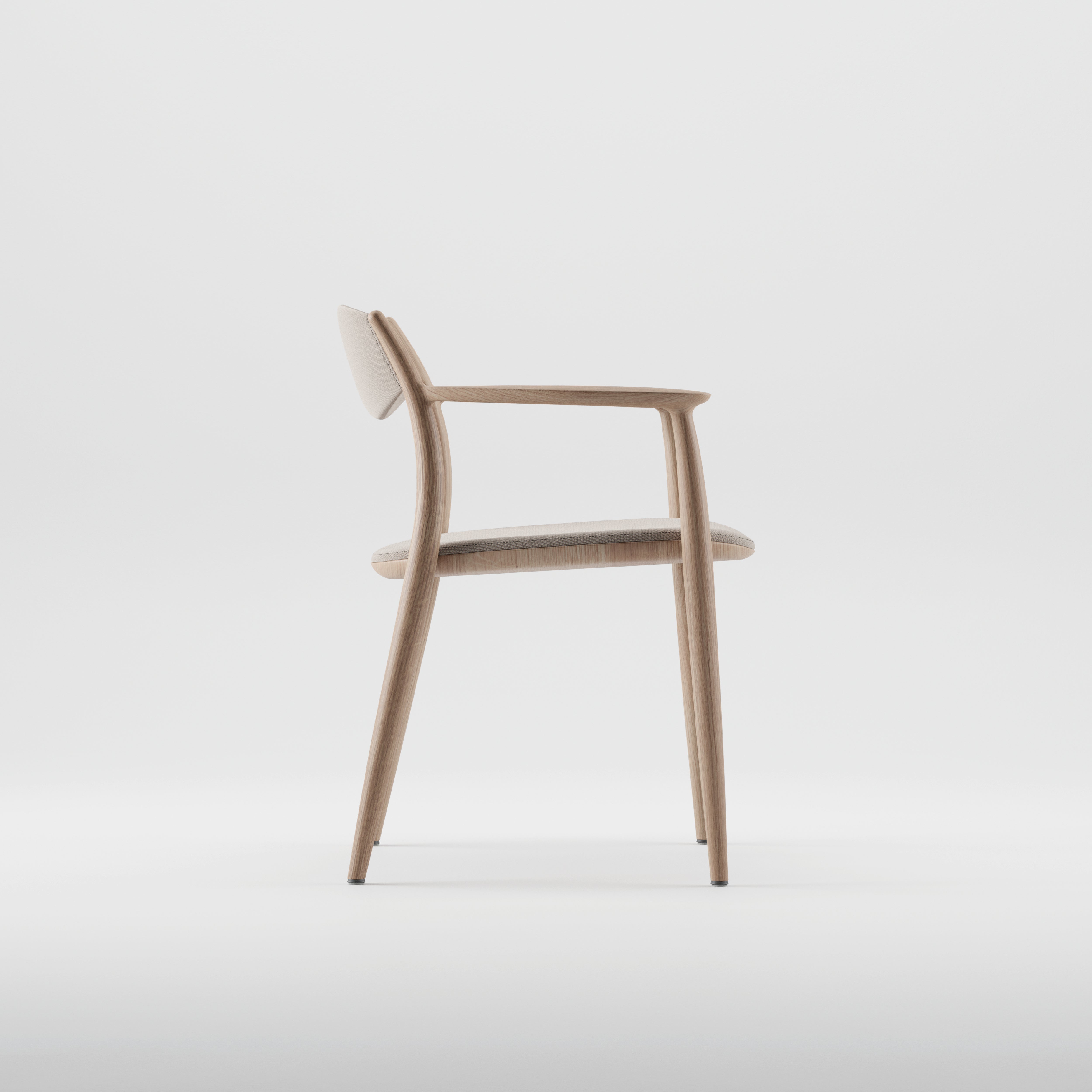 The NILA Chair by Artisan features a side view of a minimalist design, crafted from solid wood and finished with natural oils. It has a light wooden frame, upholstered backrest, and seat cushion. Slim, angled legs enhance its clean aesthetic using environmentally-friendly materials.