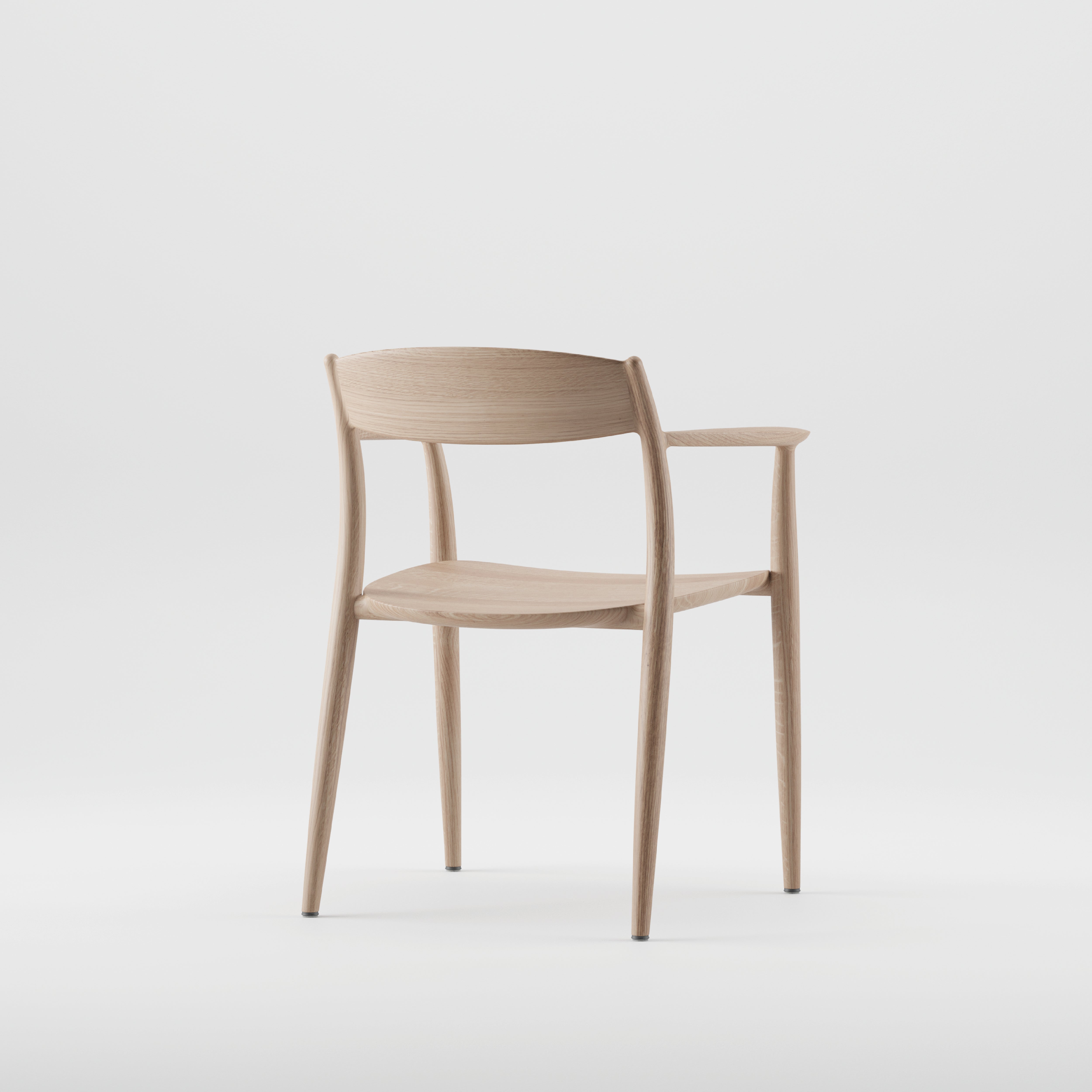 The NILA Chair by Artisan is a minimalist wooden piece with a light finish, crafted from solid wood and enhanced with natural oils. It features a curved backrest, slender legs, and simple armrests against a plain white background.