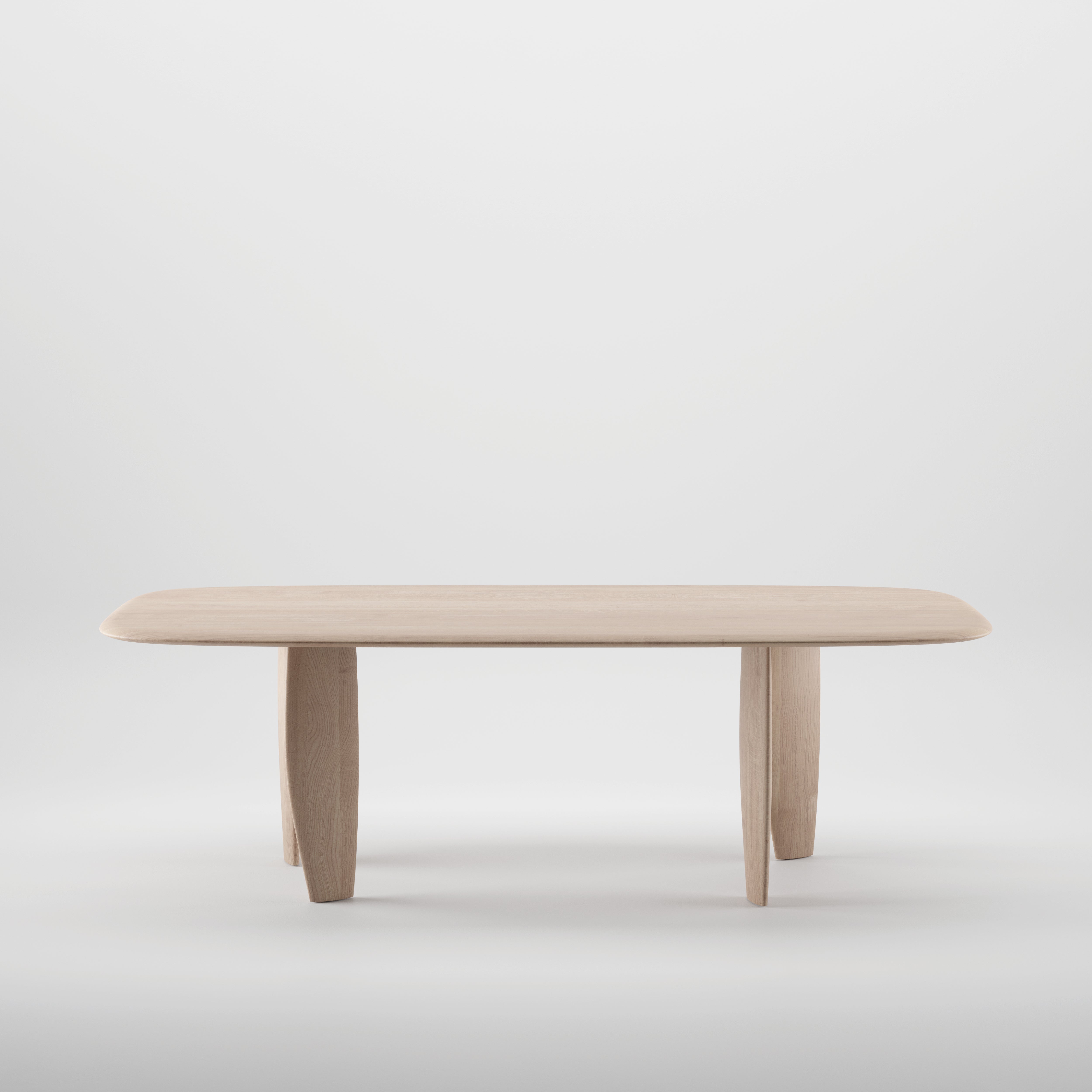The Artisan NILU Table is a minimalist wooden design made from solid wood, featuring a rectangular top with rounded edges and four slightly angled legs. Its light, natural finish shines against a plain white background, enhanced by natural oils for an eco-friendly appeal.