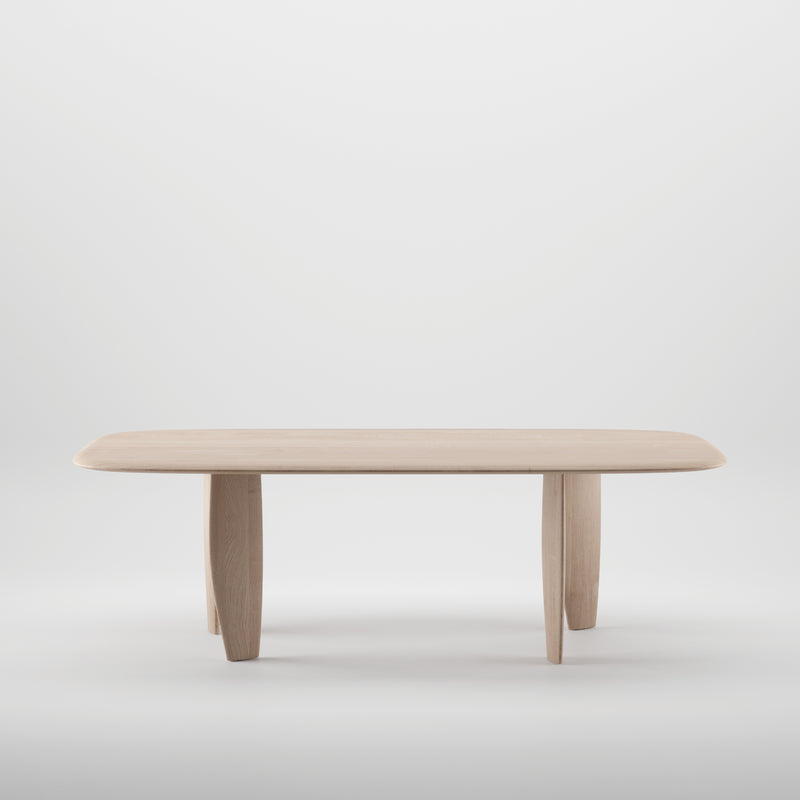 The Artisan NILU Table is a minimalist wooden design made from solid wood, featuring a rectangular top with rounded edges and four slightly angled legs. Its light, natural finish shines against a plain white background, enhanced by natural oils for an eco-friendly appeal.