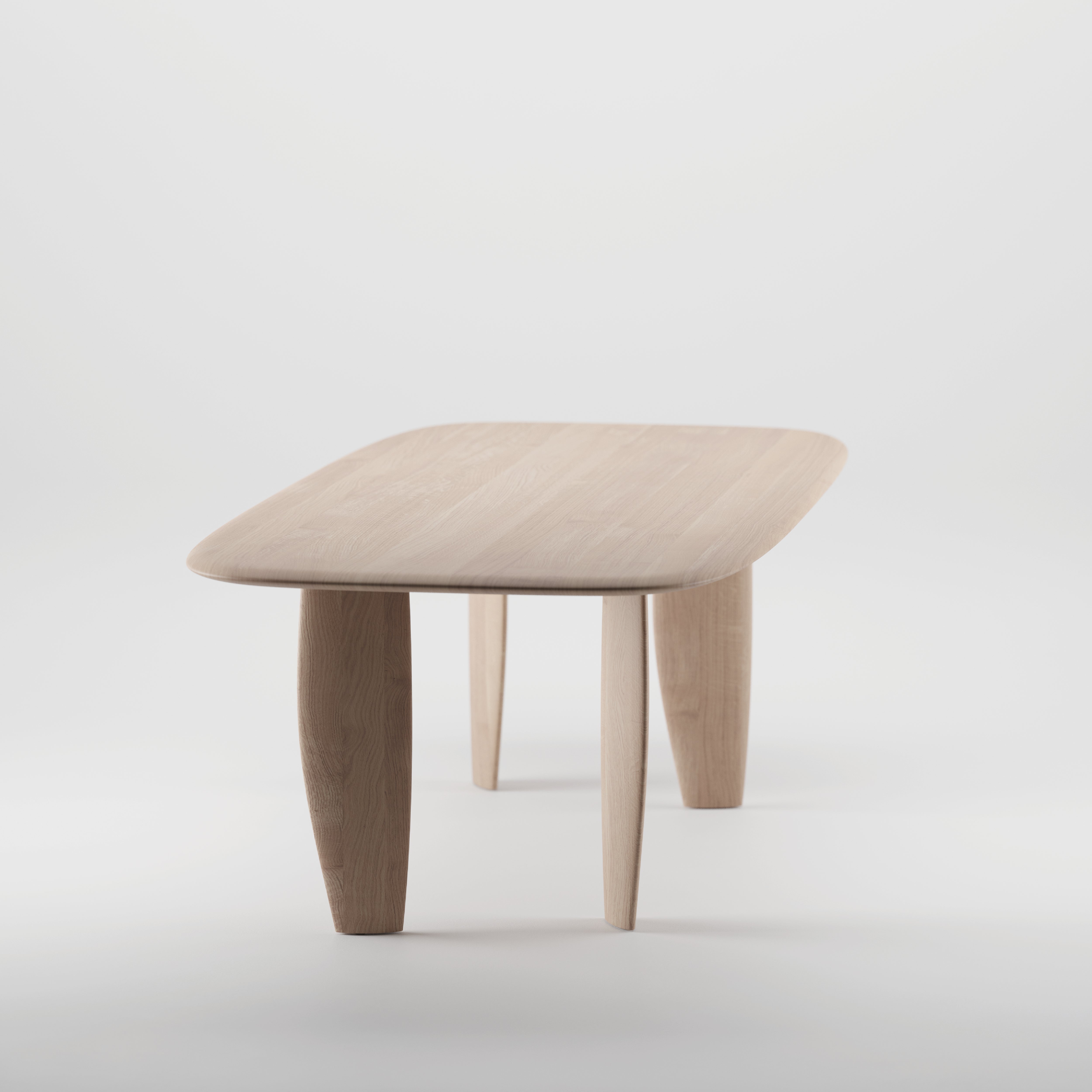 The NILU Table by Artisan is a minimalist wooden table with a solid wood rectangular top featuring rounded edges and four slightly curved legs, crafted from environmentally-friendly materials and finished with natural oils. It stands against a plain white background.
