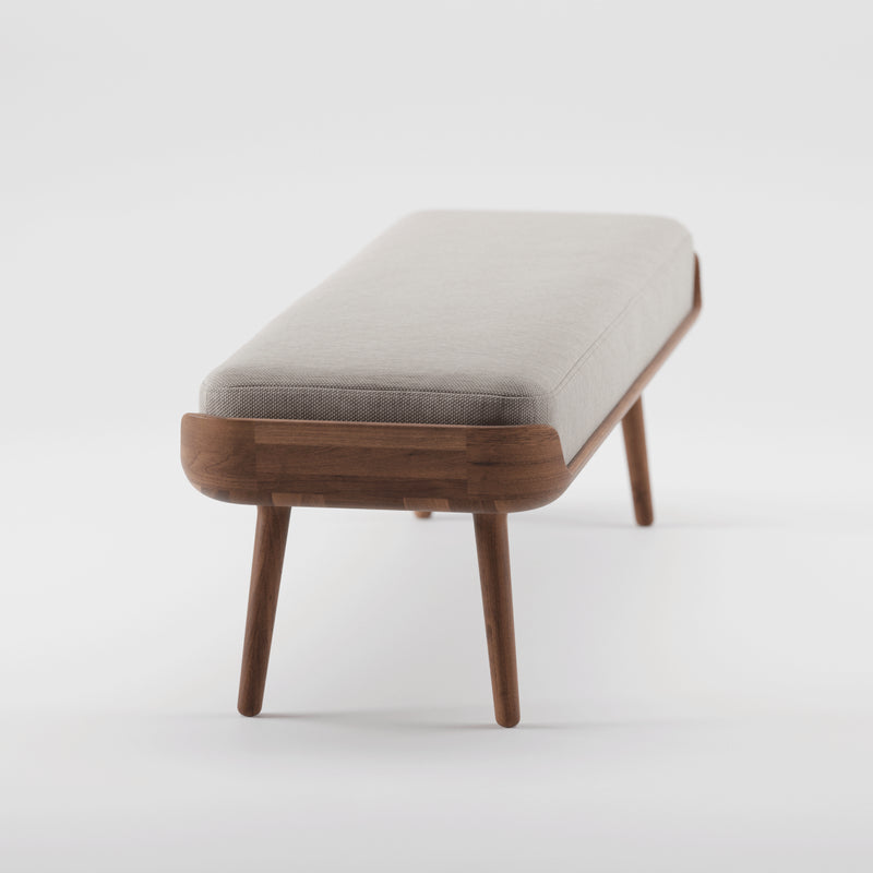 The THOR Bench by Artisan features a minimalist design with solid wood construction and a natural texture. It has four tapered legs and a light gray rectangular cushion with rounded corners, set against a white background.