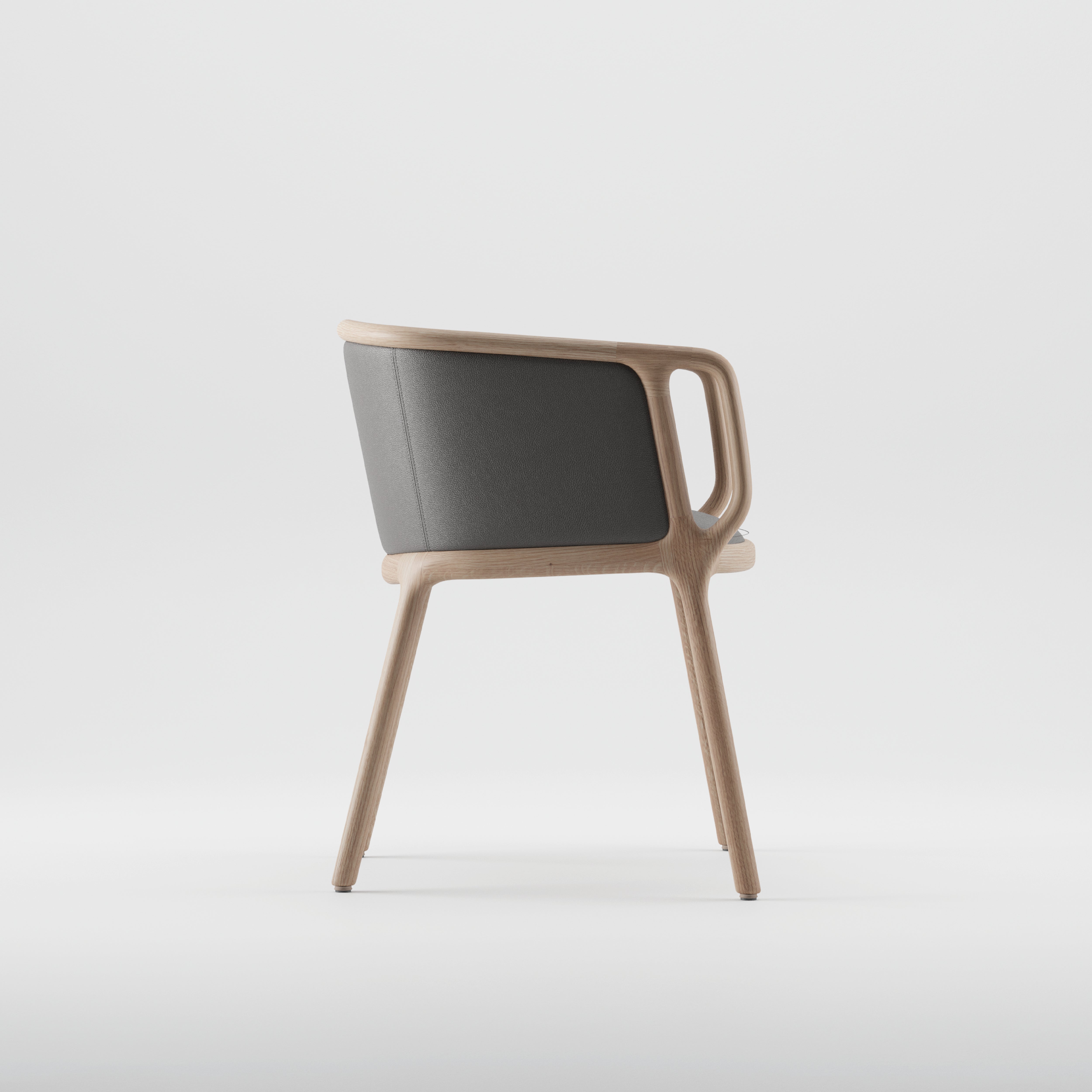 The VELO Chair by Artisan is a modern piece with a minimalist design, made from solid wood with natural oil finishes. It boasts dark gray cushioned backrests and seats, highlighting the smooth curves of its armrests and legs against a plain white background, emphasizing its elegance.