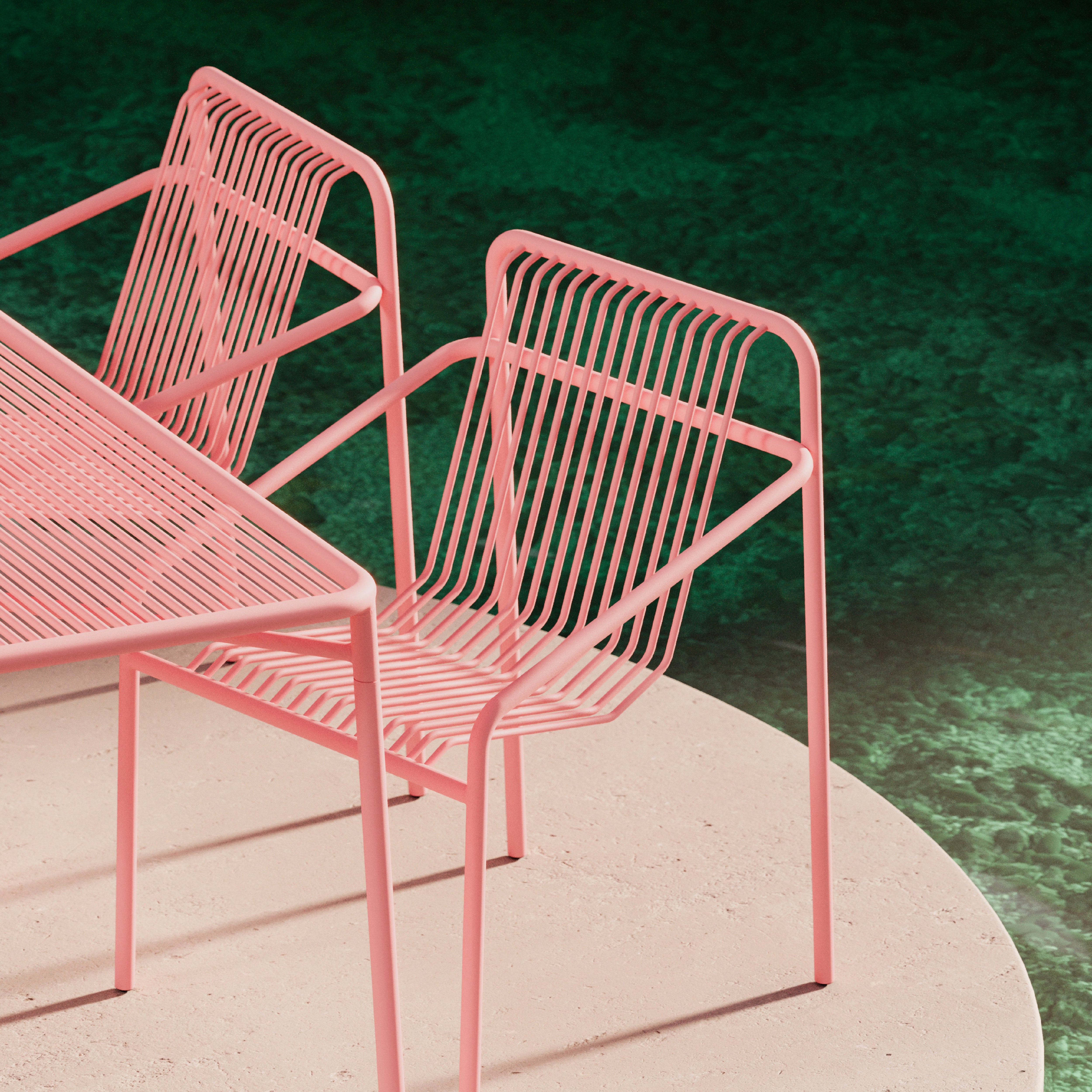 The IVY Outdoor Dining Chair by Objekte unserer Tage shows off its pink wireframe design alongside a matching angular table. The set is weather-resistant, elegantly set on a light circular surface, contrasting with the dark green background for a blend of style and durability.