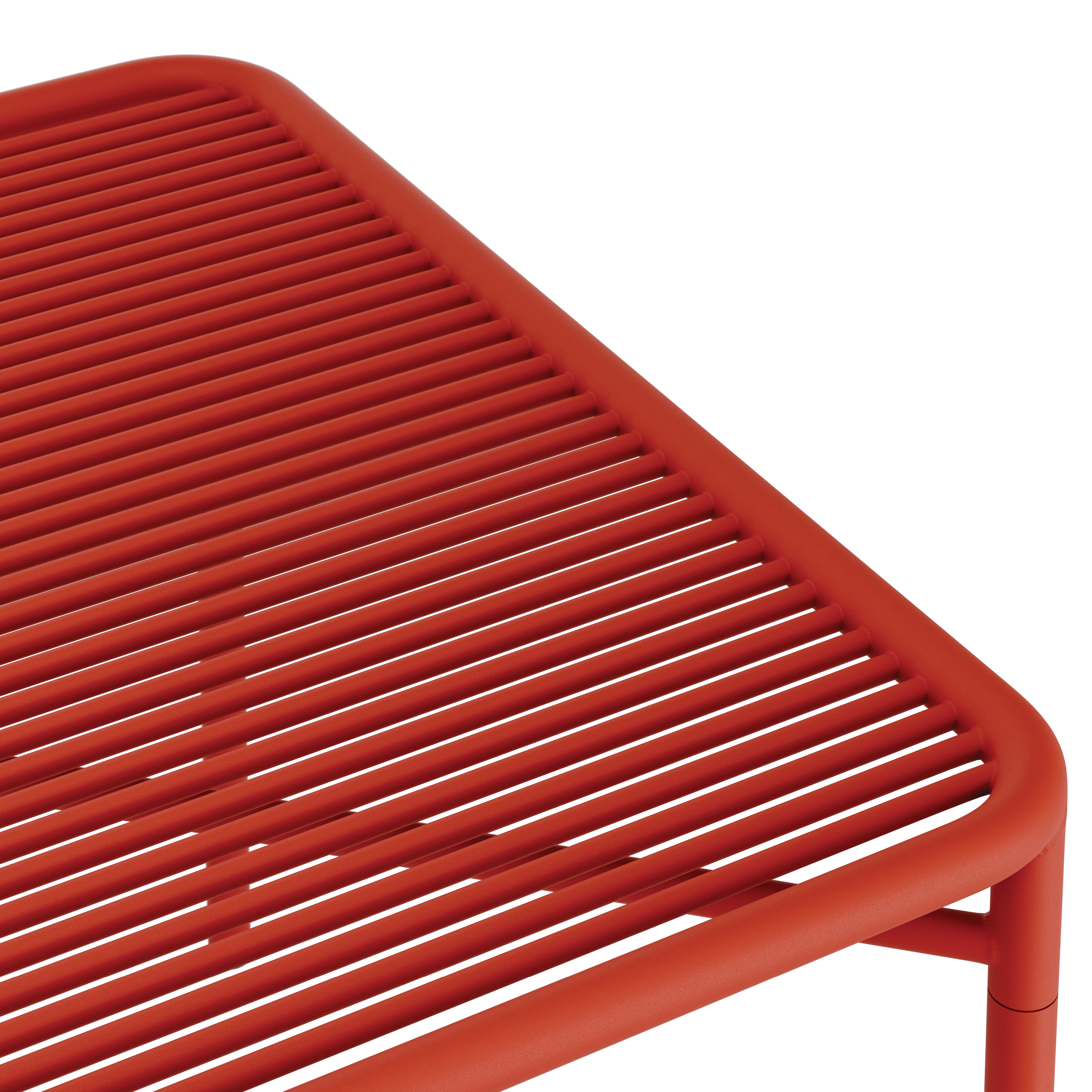 The IVY Outdoor Table by Objekte unserer Tage is a red metal table crafted from powder-coated steel featuring a slatted top, rounded edges, and cylindrical legs. Its modern design casts subtle shadows, highlighting its sleek and minimalist style.