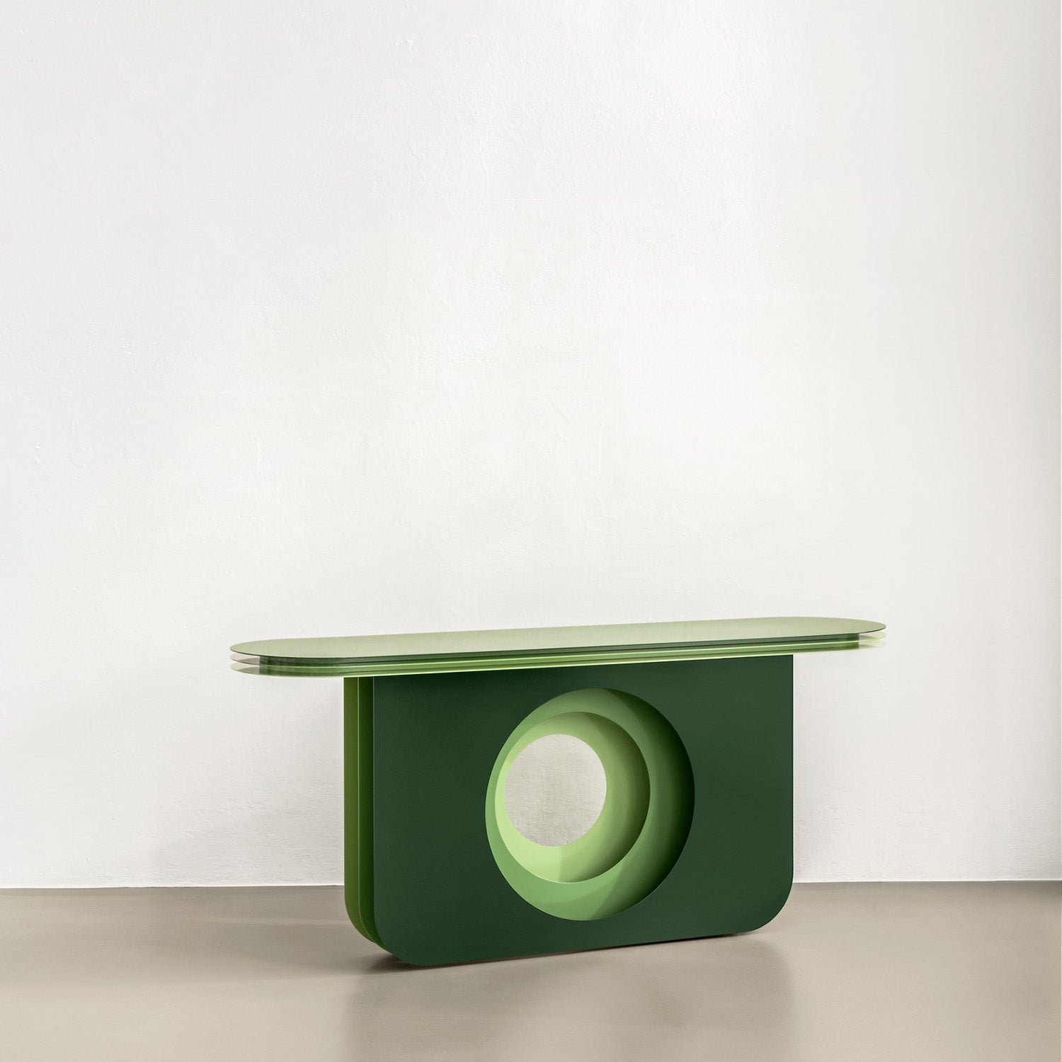 The My Ami Sideboard by Victor Foxtrot is a modern green console table crafted from powder-coated steel, featuring an oval top and a thick base with a circular cutout, set against a light gray background for style and visual depth.