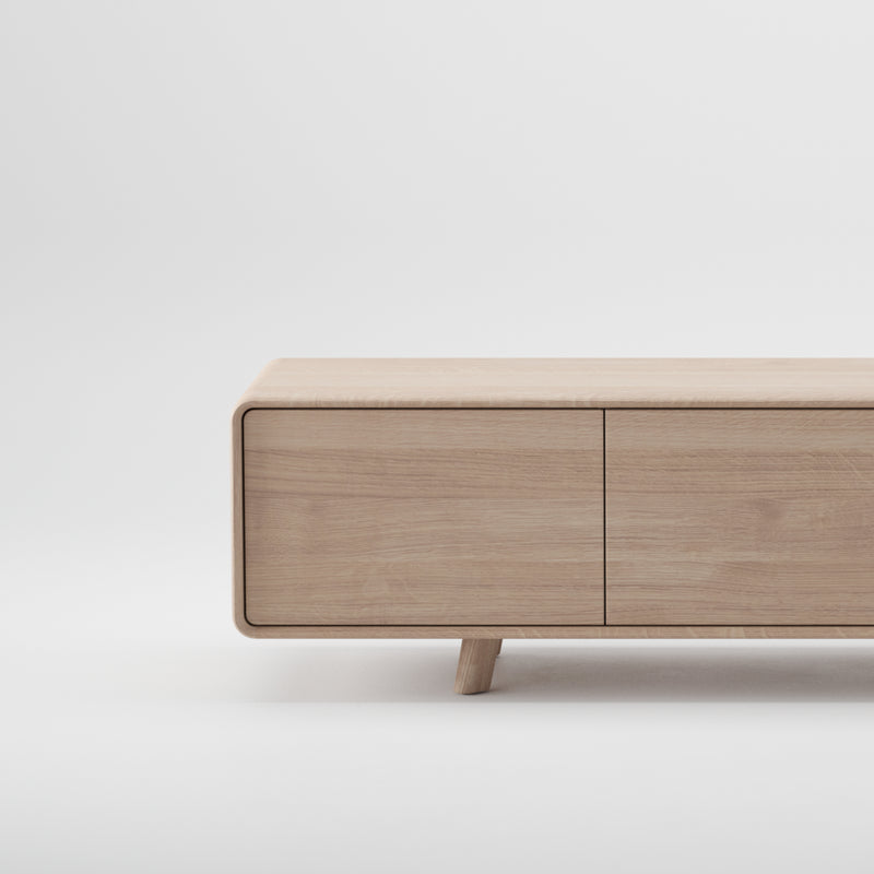 The NEVA Lowboard by Artisan is a minimalist bench crafted from environmentally-friendly solid wood with a light natural finish. Featuring a smooth, flat surface, rounded edges, and short tapered legs on a white background, it exudes sustainable elegance.
