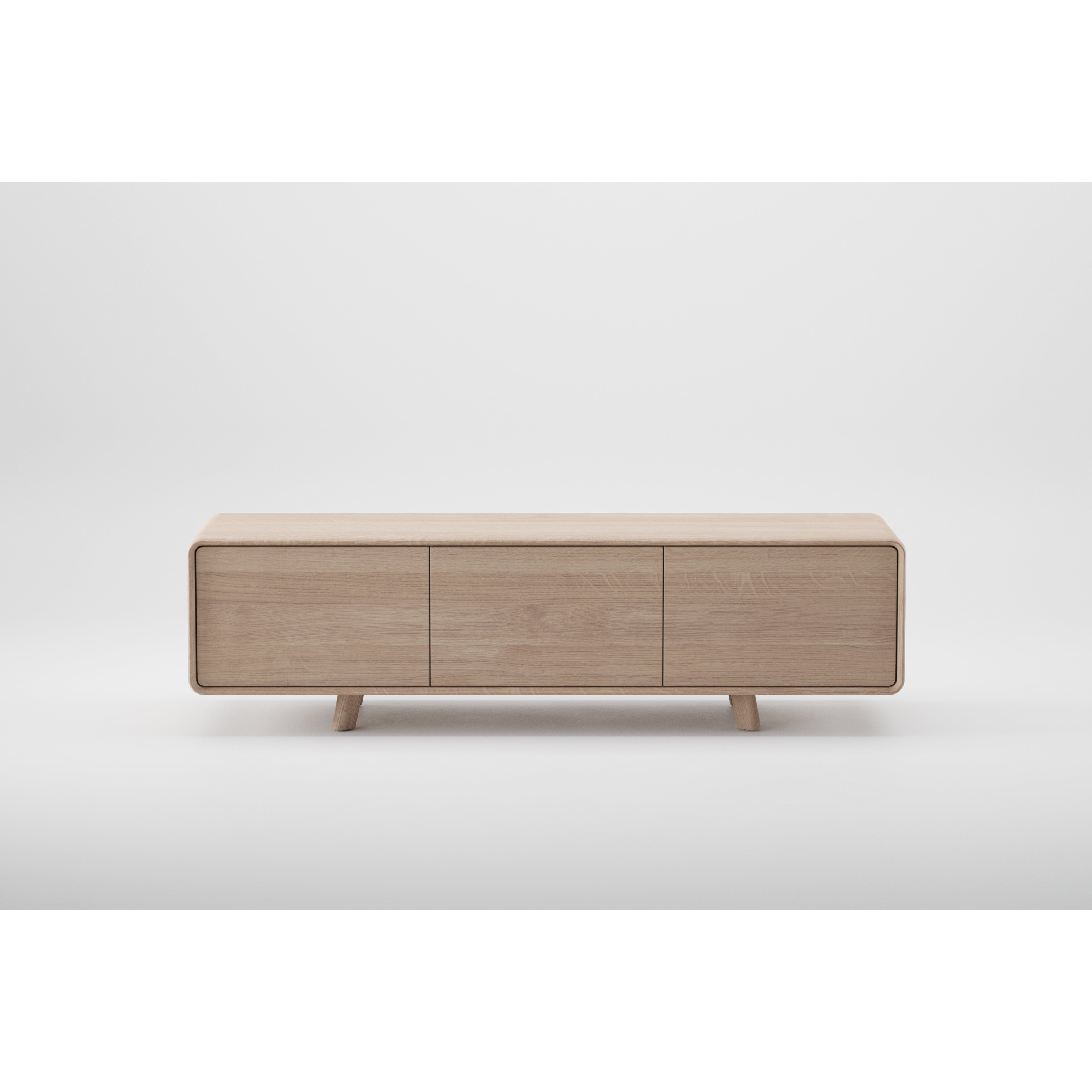 The NEVA Lowboard by Artisan is a modern, minimalist TV stand crafted from solid wood and finished with natural oils and wax. It features three front panels, short tapered legs, and a streamlined design made with environmentally-friendly materials, perfect for contemporary interiors.