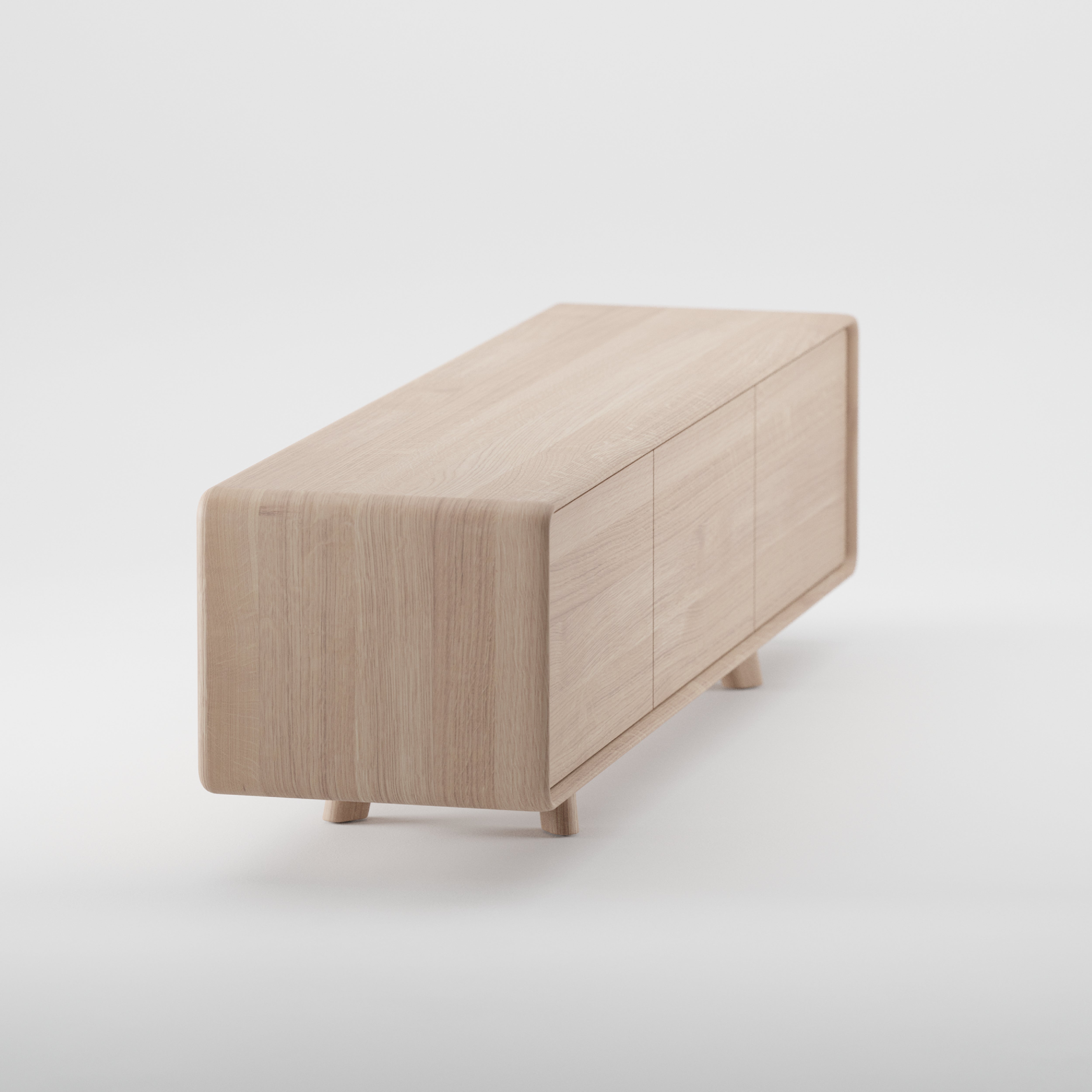 The Artisan NEVA Lowboard is a minimalist wooden sideboard made from eco-friendly materials with a light, natural finish. It has smooth, rounded edges and small legs, and features three seamless cabinet doors for a sleek, modern design.