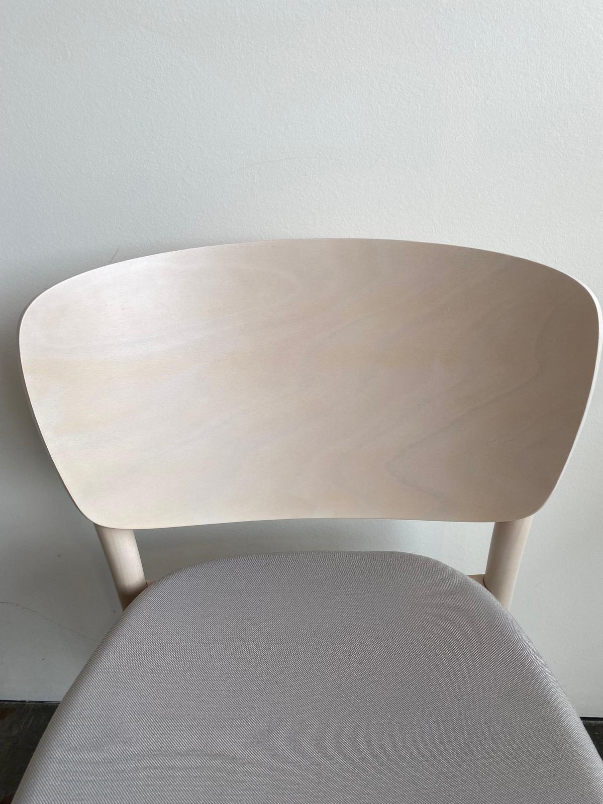 The Chair Valencia Upholstered by TON is a minimalist wooden chair with solid construction, featuring a smooth, light-colored backrest and cushioned seat. This timeless piece is ideal against a plain, light-colored wall.