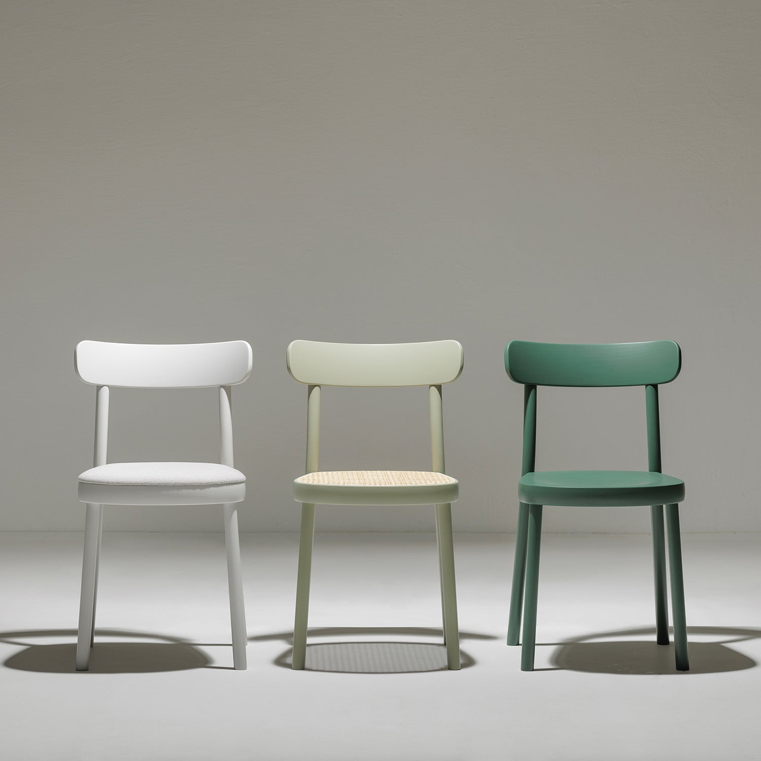 Against a plain background, three TONs Chair La Zitta - Upholstered dining chairs stand side by side, showcasing a modern design with ergonomic curved backrests and sturdy legs crafted from durable solid wood in white, pastel green, and dark green.