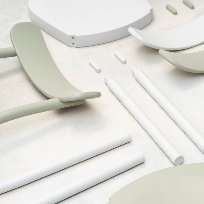 Scattered on a light surface are parts of the Chair La Zitta - Upholstered from TON, including green and white curved sections, cylindrical rods, and small connectors. The dining chair features an ergonomic design with a modern, minimalistic style.
