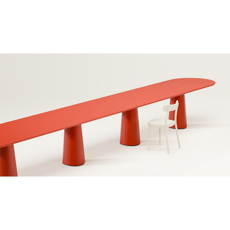 The P.O.V. Plus Table 481 by TON is a minimalist red table featuring rounded edges and cylindrical legs, ideal for both office and dining settings. It includes a single white chair placed to the right against a light background.