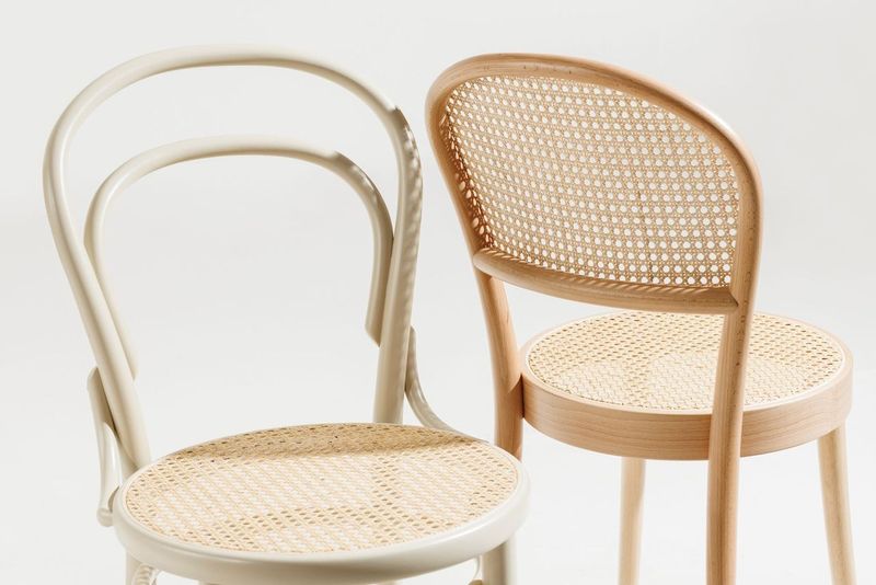 The TON Chair 314-Cane by TON showcases exquisite bentwood craftsmanship with woven cane seats and backs. One is painted white with a rounded backrest, while the other features a natural wood finish and rectangular backrest, both perfectly suited for a minimalist setting.
