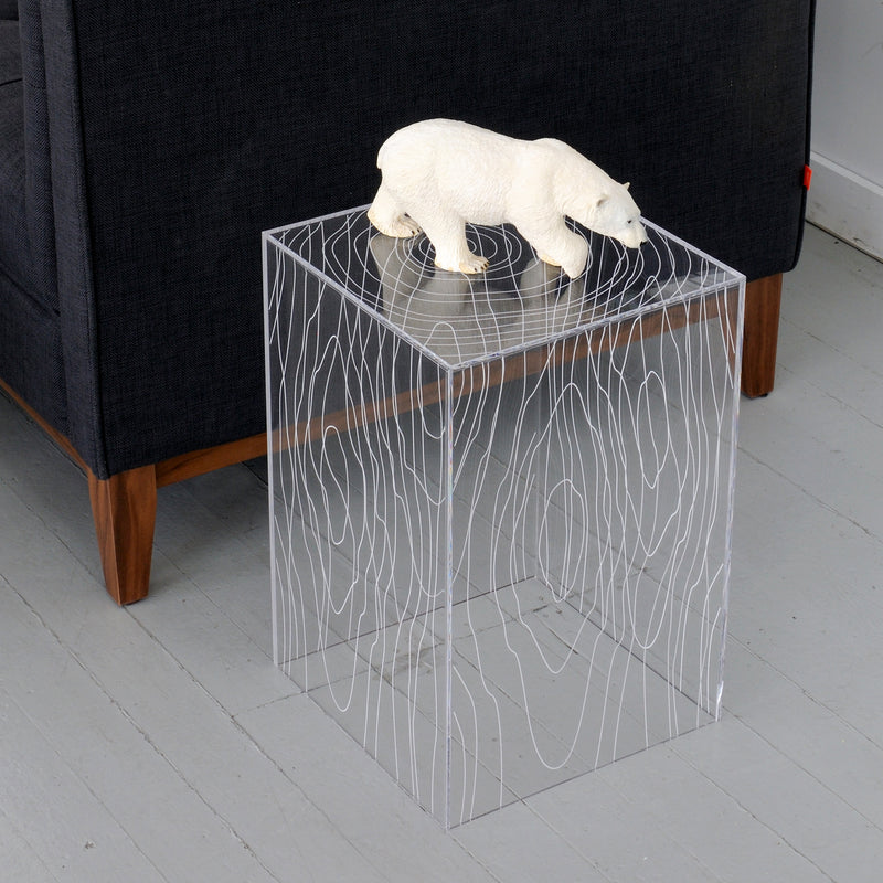 Clear acrylic side table with white woodgrain pattern and white polar bear figurine on top next to dark fabric sofa