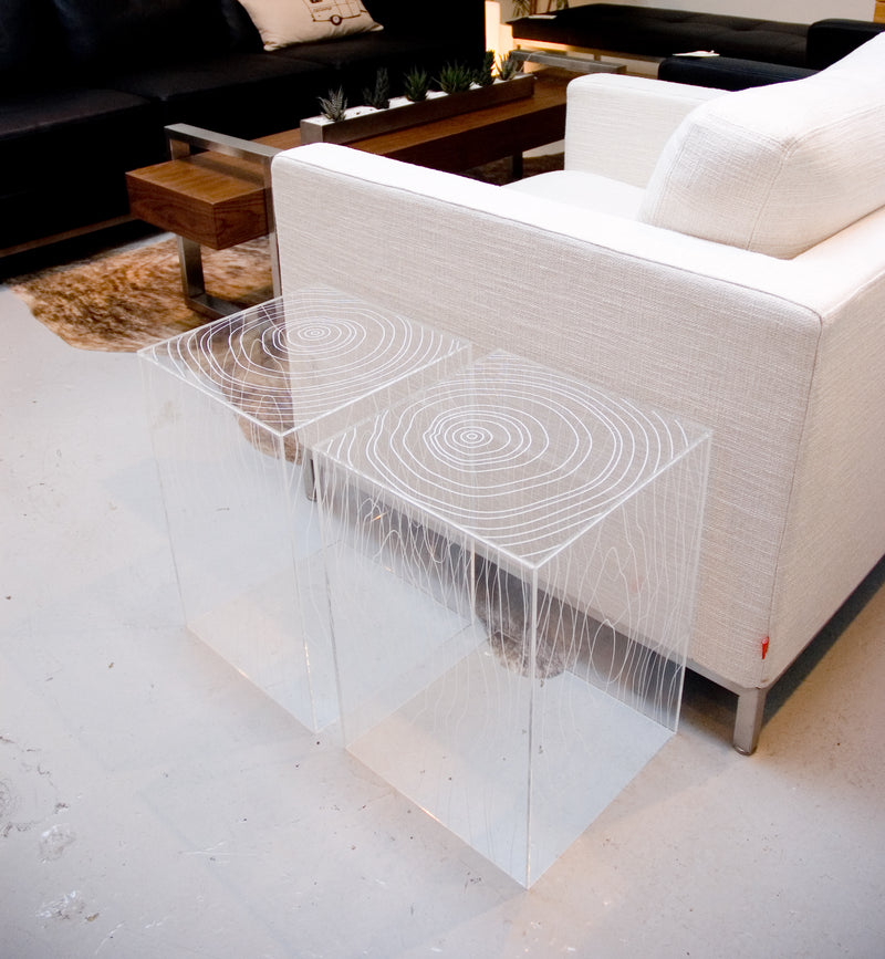 Pair of clear acrylic cube side tables with white tree ring pattern beside white fabric armchair on concrete floor