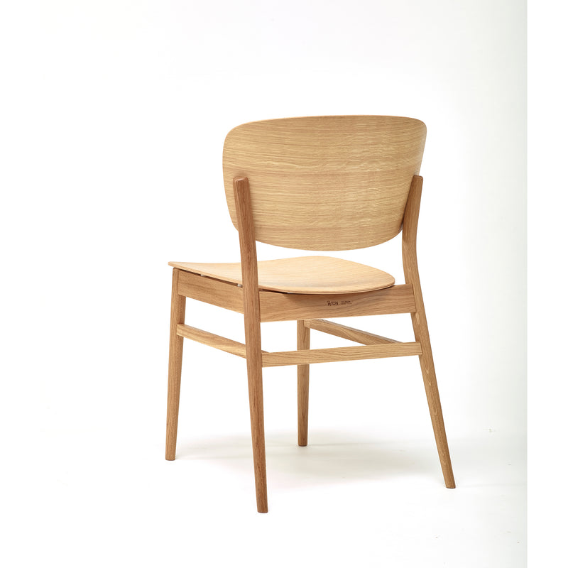 The Chair Valencia by TON is showcased against a white backdrop, highlighting its minimalist design with a smooth, curved backrest, flat seat, and straight legs. Crafted from solid wood, its natural grain and ergonomic form are prominently featured.