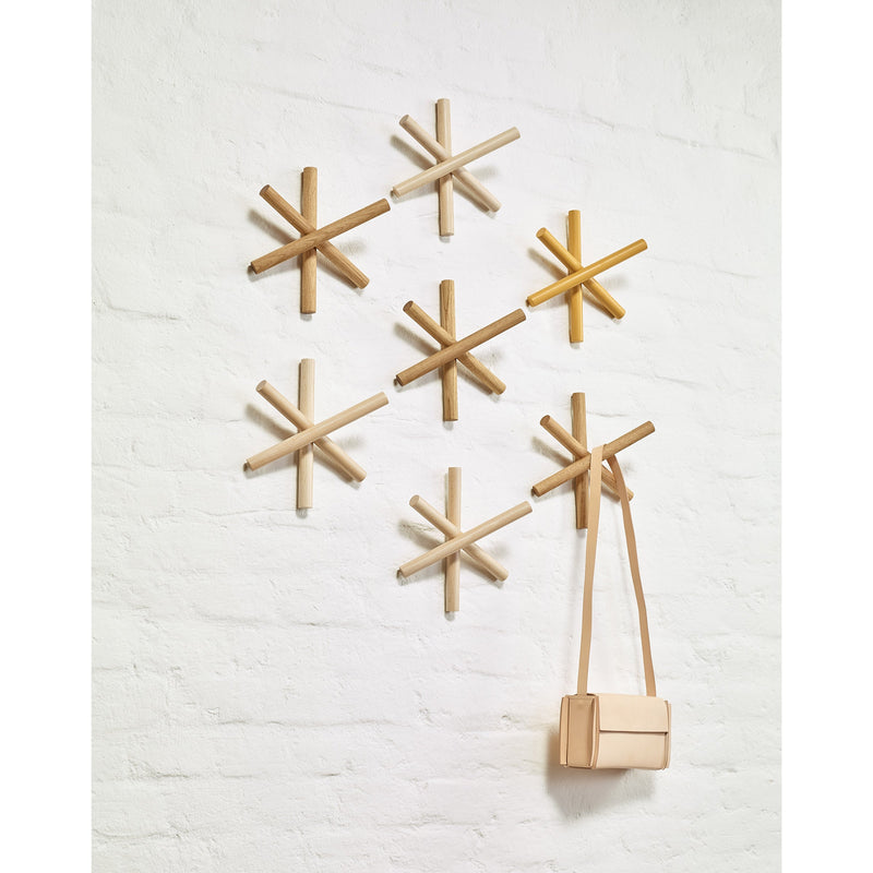 Logs - Inventory by TON are wooden hexagon-shaped wall hooks made from quality wood offcuts. Arranged on a white brick wall, one hook stylishly holds a tan purse with a strap, showcasing varying wood tones for a sustainable design and captivating geometric aesthetic.