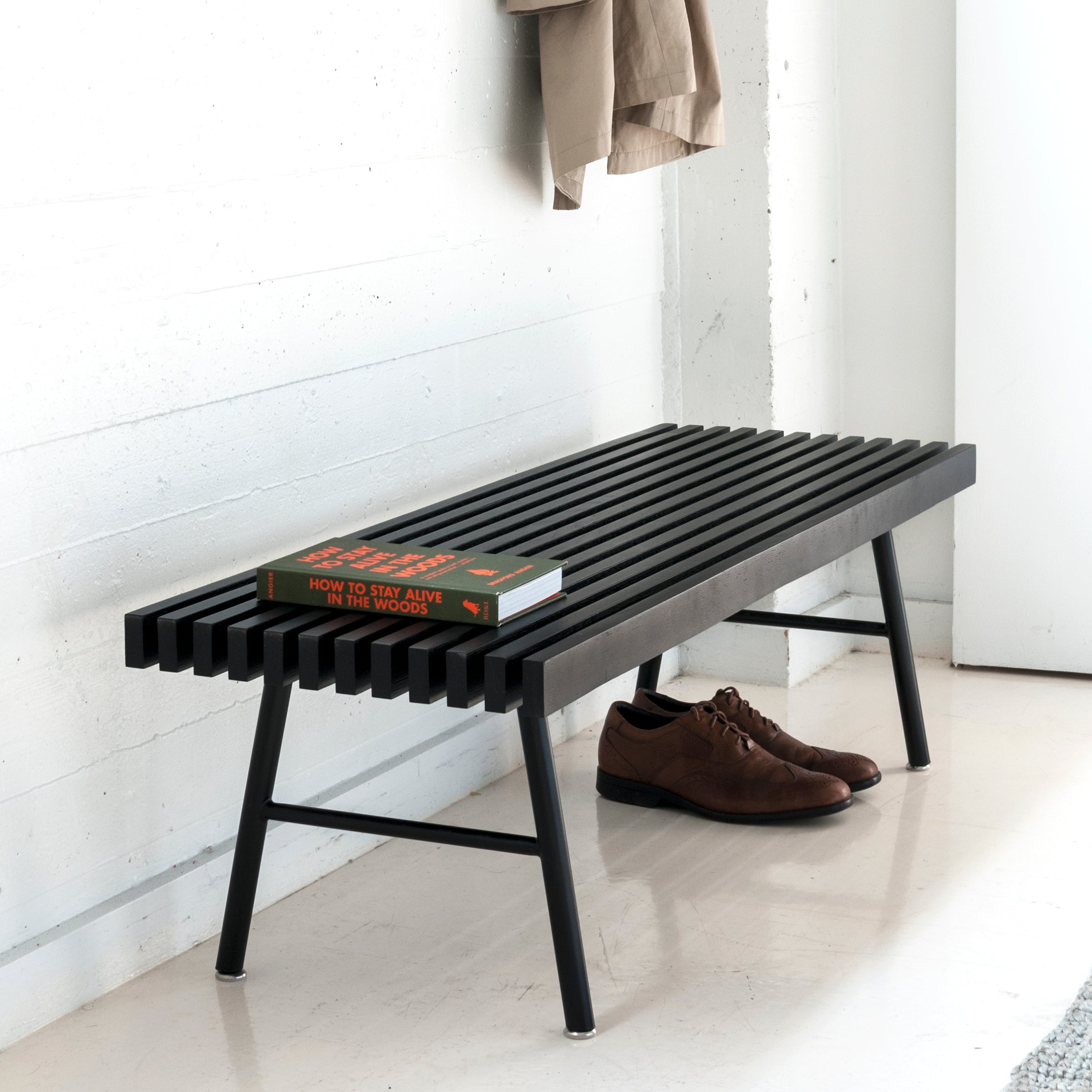 Black metal bench with a book on a white floor against a white wall.
