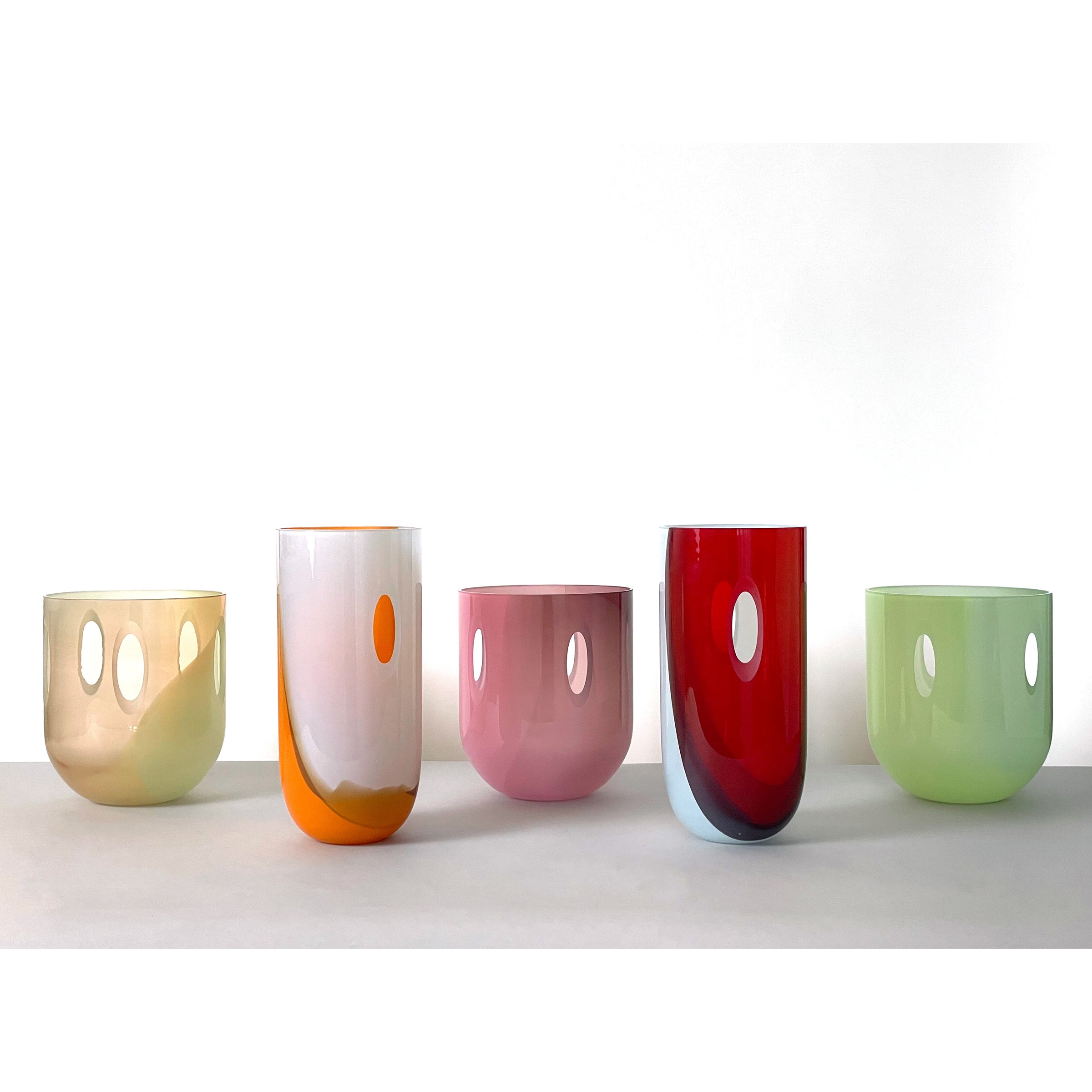 Five colorful ECLIPSE Vases by Ursula Futura, crafted from mouth-blown glass with unique oval cutouts, display a spectrum of pastel and vibrant tones against a plain white background.