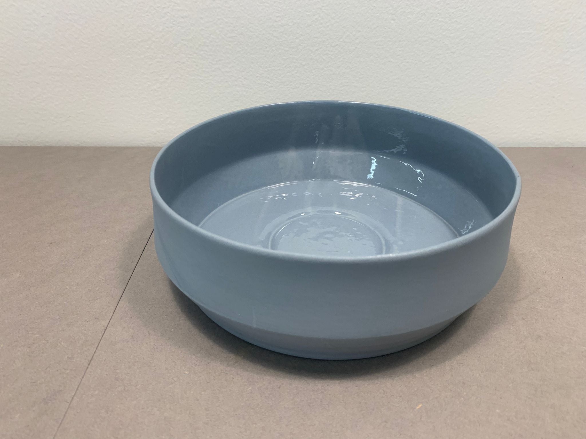 The Unison Soup Bowl, a gray ceramic piece by Schneid, showcases its smooth, minimalist design under soft lighting that reveals depth and texture. Handmade in Germany, it rests elegantly against a light, neutral backdrop.