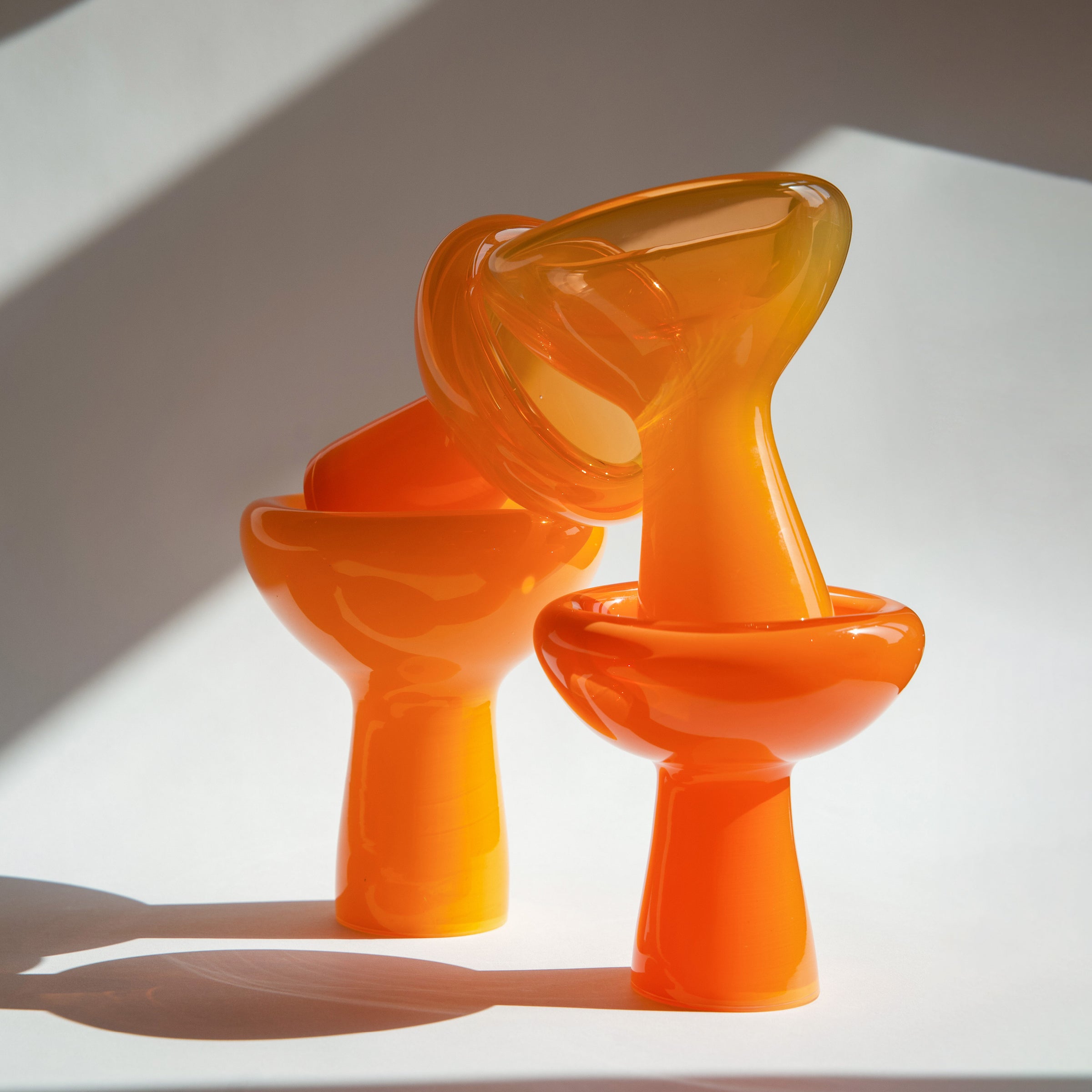 Two glossy, curved orange sculptures with smooth surfaces, echoing the distinctive style of Ursula Futuras PHANTOM Dish, are artistically stacked against a neutral backdrop, creating soft shadows.