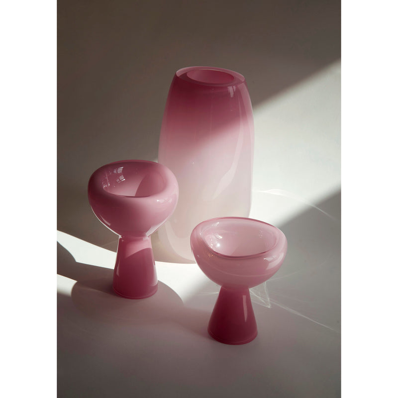 Three PHANTOM Dish pieces by Ursula Futura, crafted from pink mouth-blown glass in varying sizes and shapes, are softly illuminated against a neutral backdrop. The unique design casts gentle shadows on the surface, creating an ethereal ambiance.