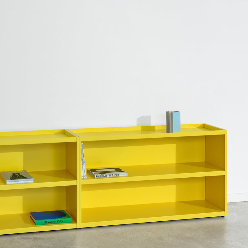 Set against a white wall, the Loehr W1 Stack Shelves exude a minimalist aesthetic with its bright yellow two-compartment design. The books scattered amid its lines complement the polished concrete floor, highlighting its sleek industrial charm.