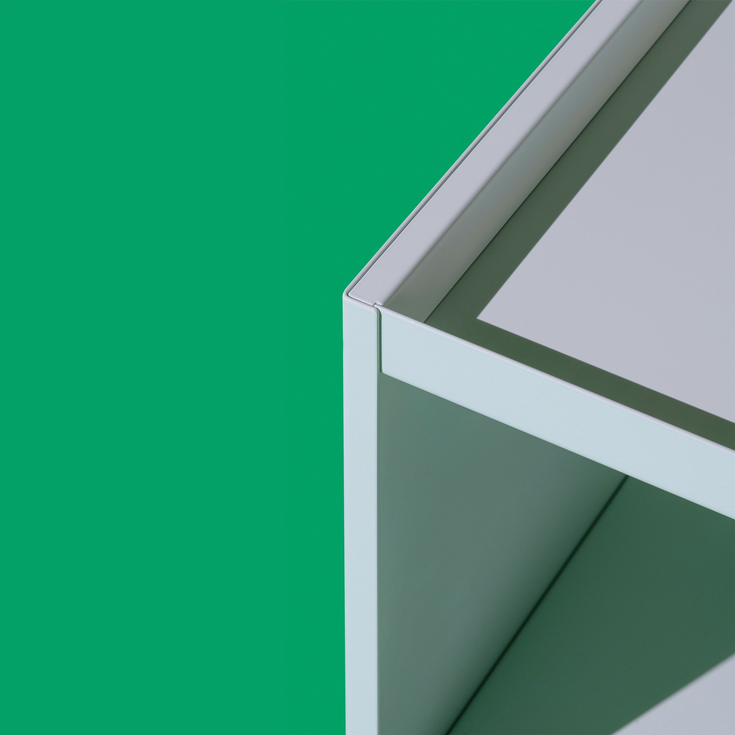 Close-up of Loehrs W1 Stack Shelves in white metal, showcasing its modern industrial design against a solid green background. The sharp edges and clean lines of this modular piece contrast strikingly with the vibrant green backdrop.