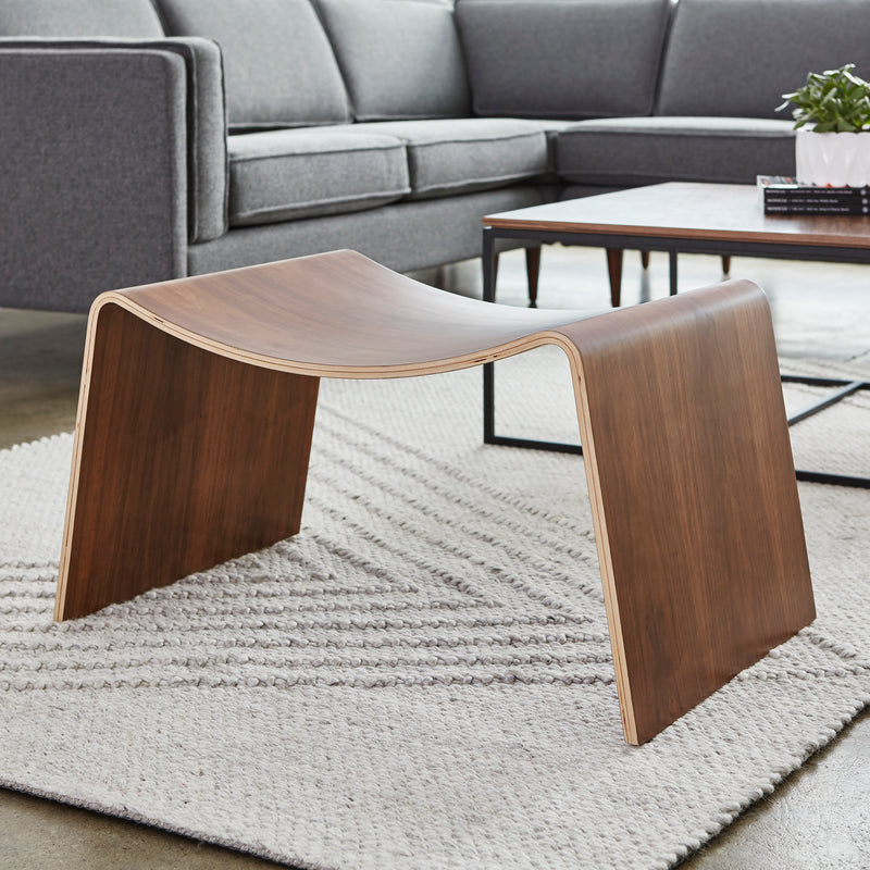 Curved walnut wood bench with smooth edges and minimalist design on textured gray rug in modern living room